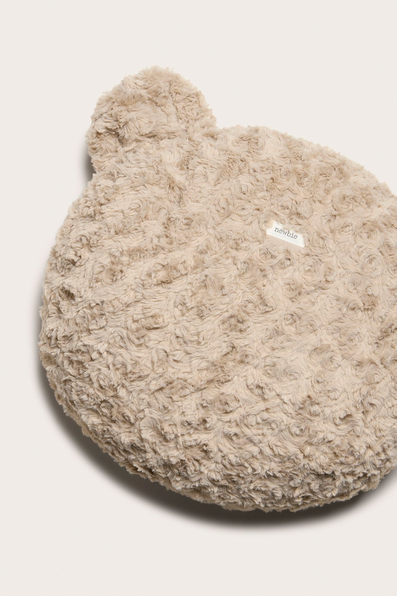 Nærbilde av en beige, lodden polyesterpile-pute formet som et bjørnehode med ører.