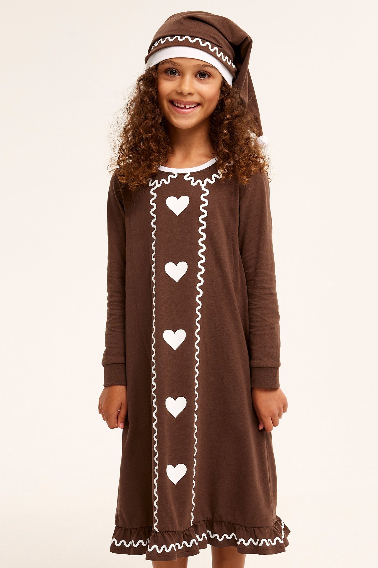 Forfra: Barn i brun pepperkakenattkjole med hvite hjerter, bølgete kant og matchende lue.