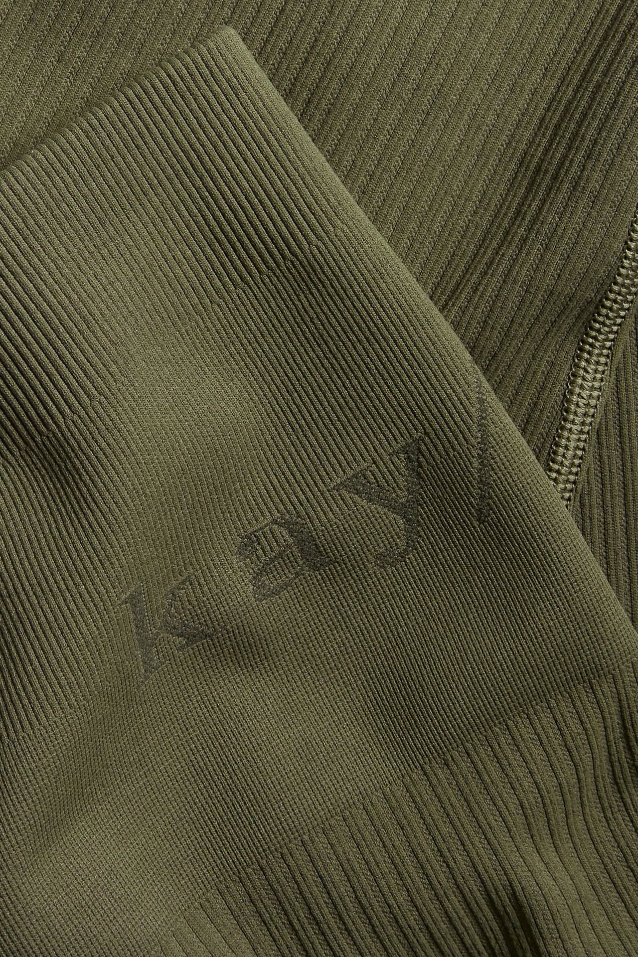 Zbliżenie zielonych prążkowanych legginsów treningowych z subtelnym wytłoczonym logo i widocznym szwem.