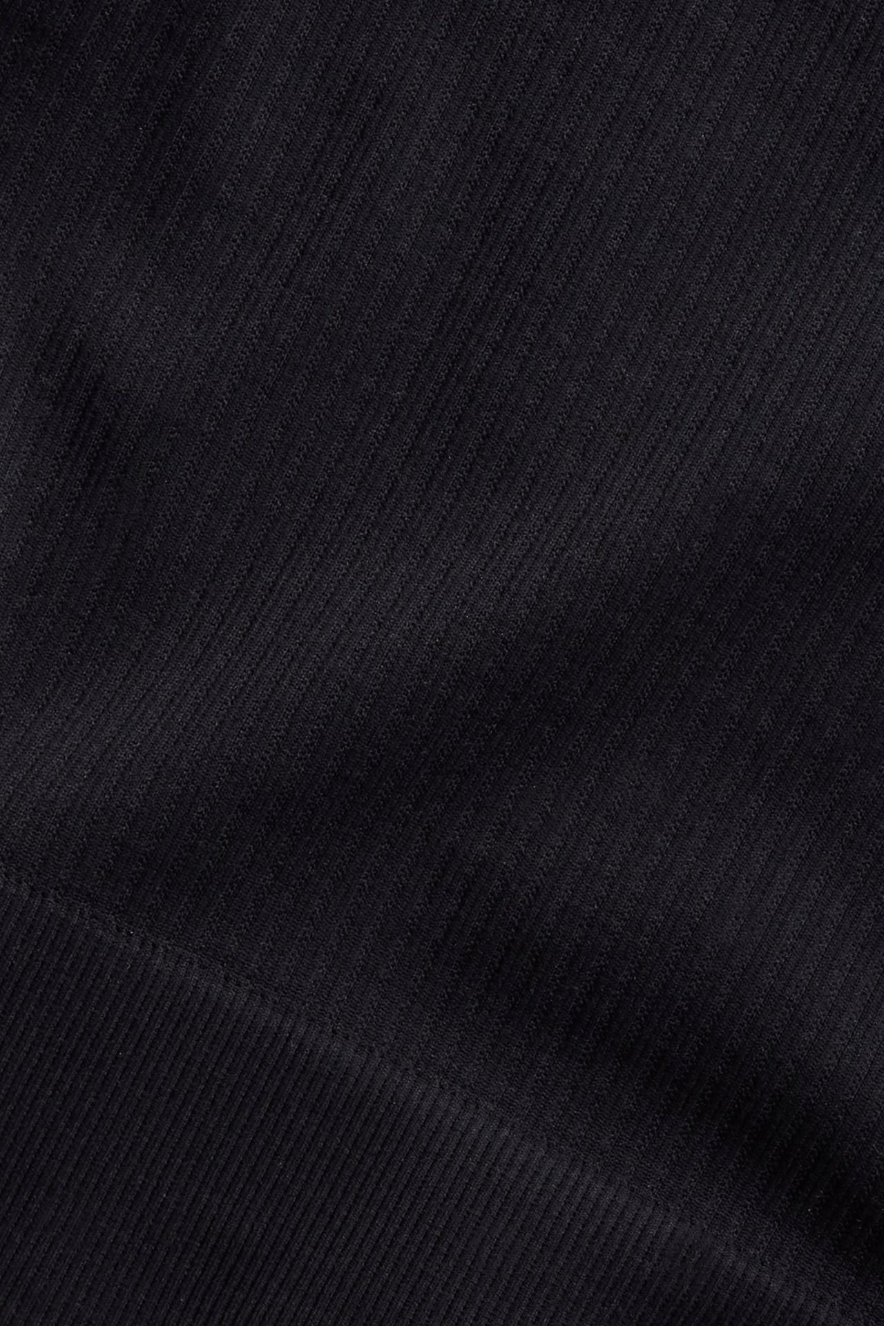 Nærbilde av svart sømløst stoff med diagonale og horisontale ribber, del av en asymmetrisk sportstopp.