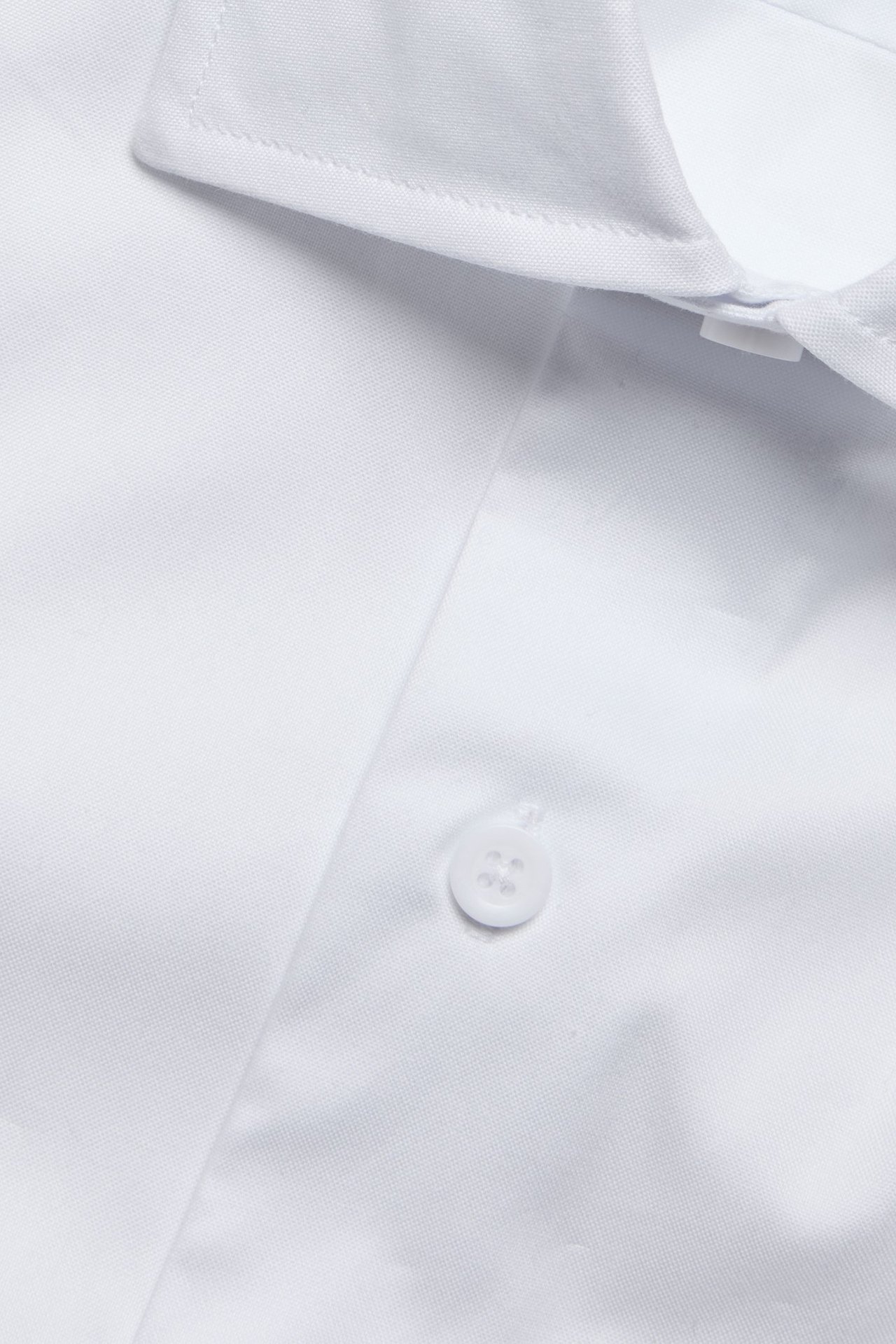 Zbliżenie białej, bawełnianej koszuli męskiej slim fit z kołnierzykiem i guzikiem.