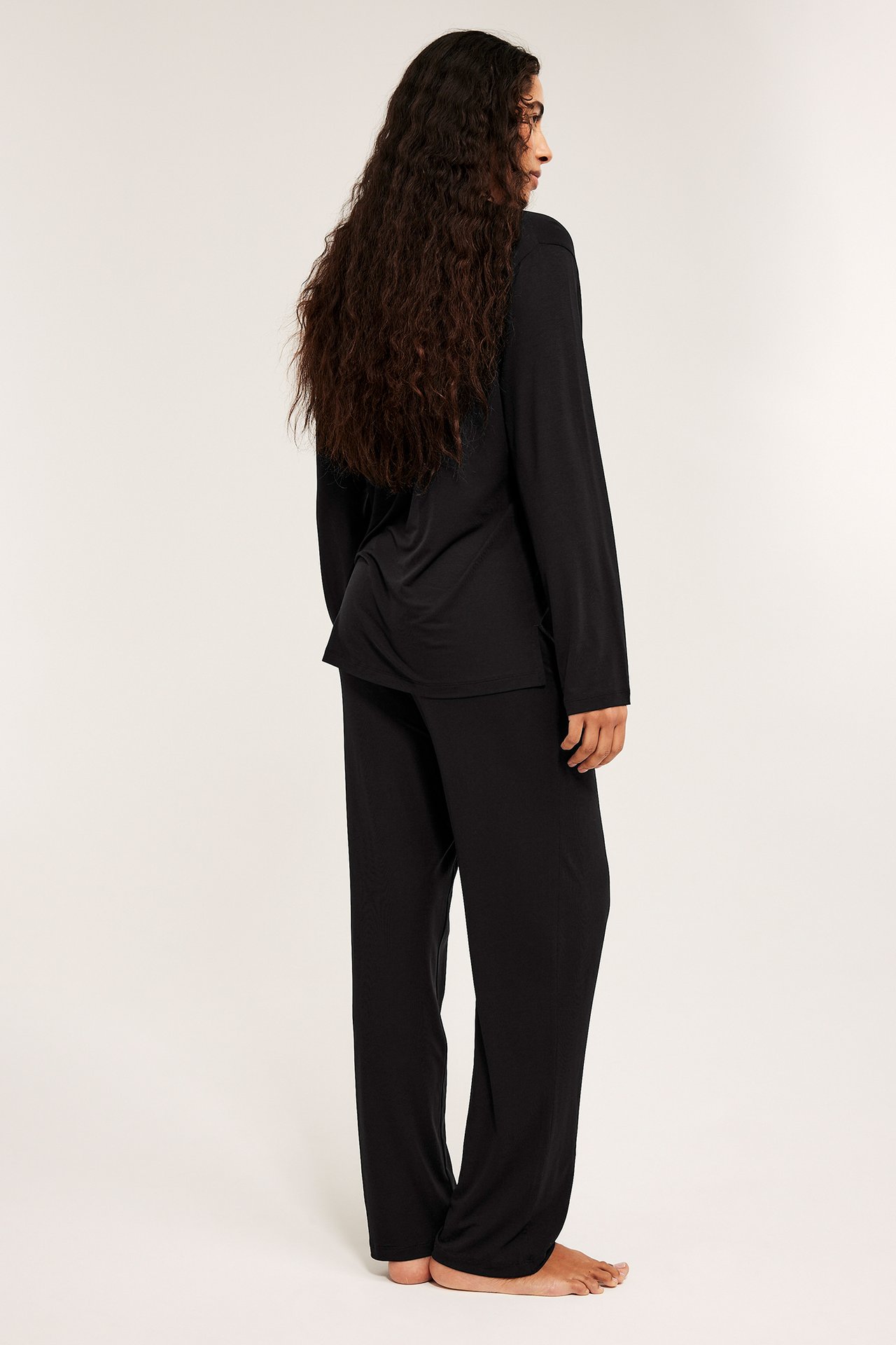 Nainen mustassa lyocell-pyjamasetissä sivulta takaa: väljä A-linjainen toppi ja suorat housut.