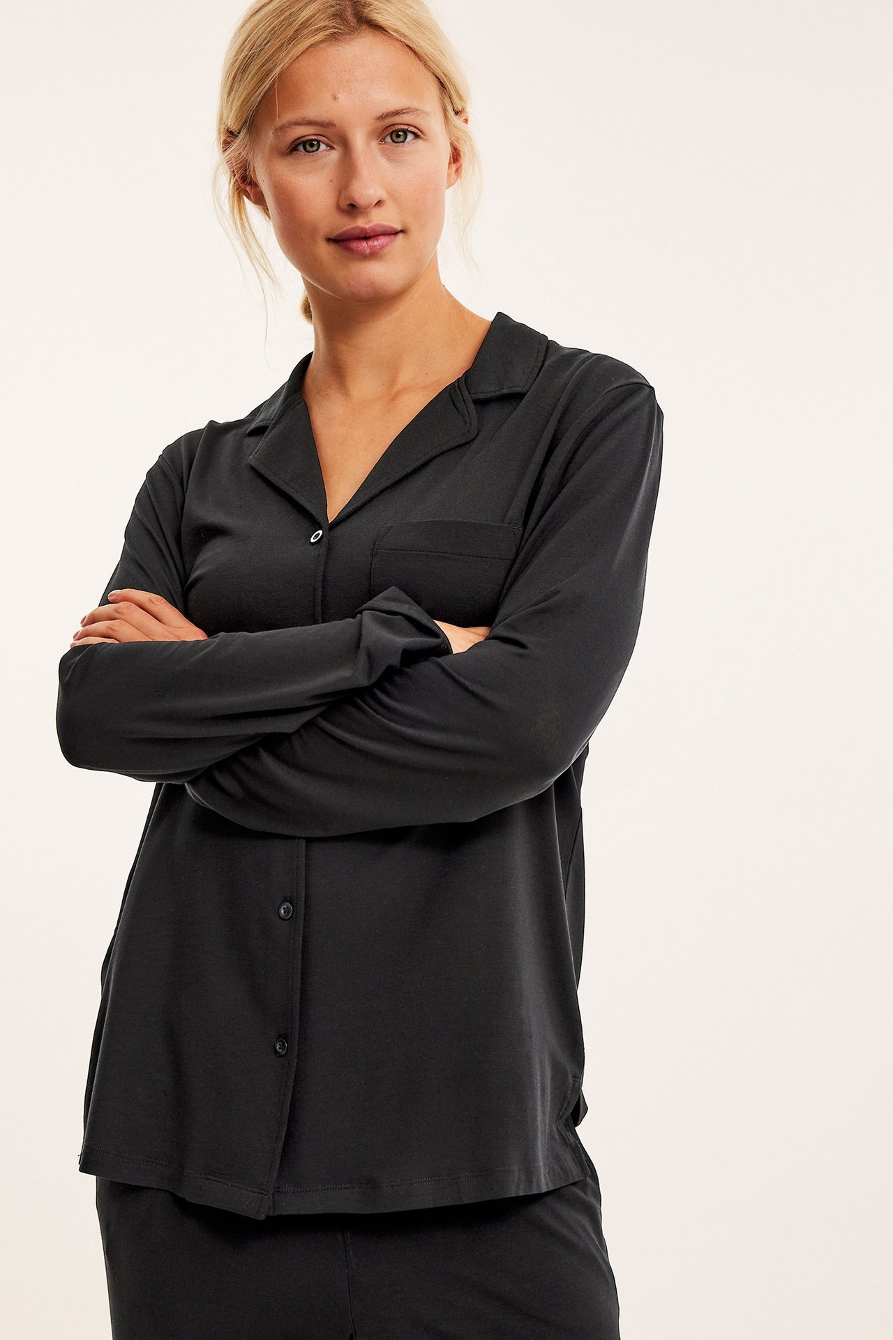 Edestä, nainen mustassa lyocell-pyjamassa, jossa pitkähihainen nappipaita ja housut.