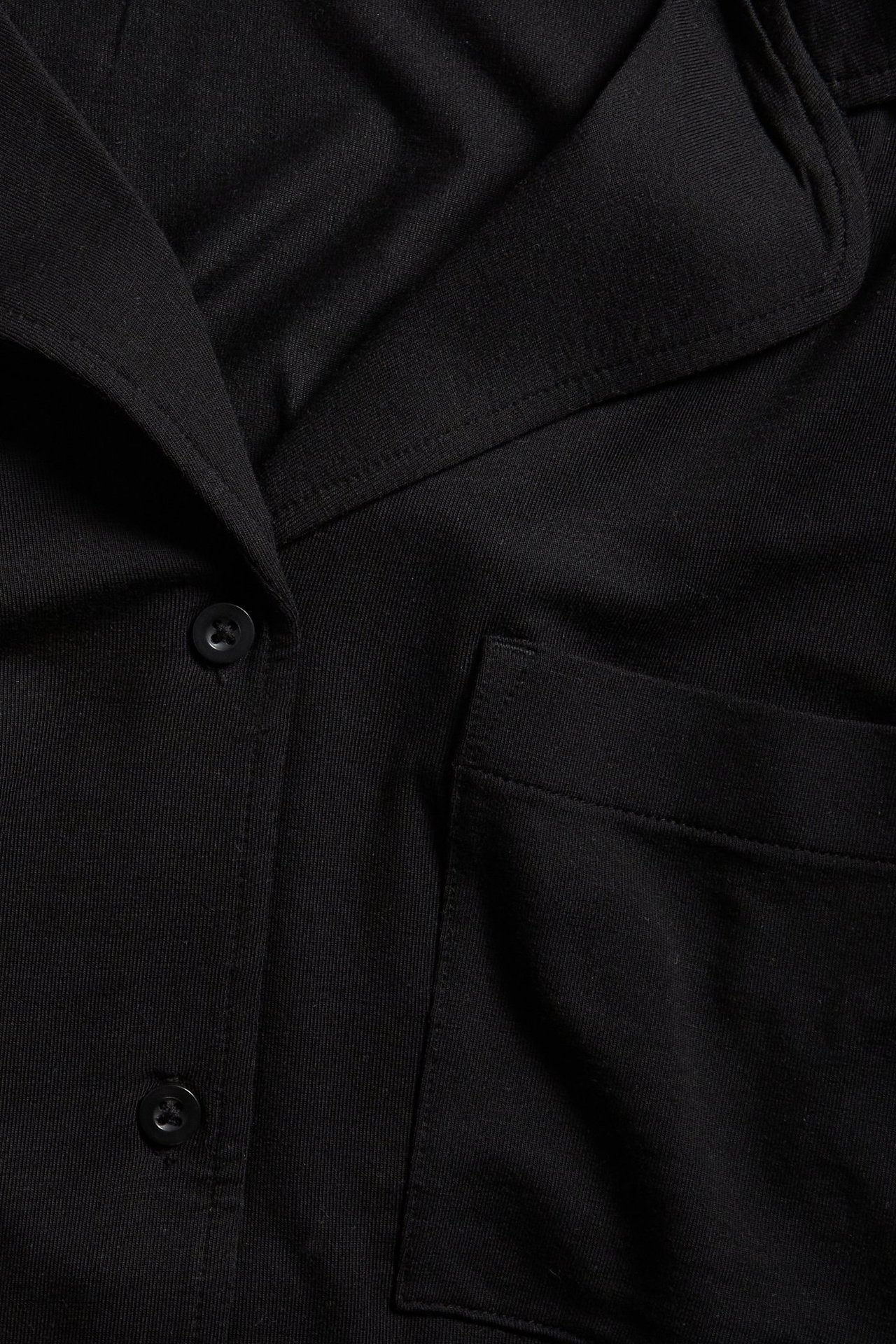 Zbliżenie czarnej koszuli piżamowej z lyocellu z kołnierzem, guzikami i kieszenią na piersi.