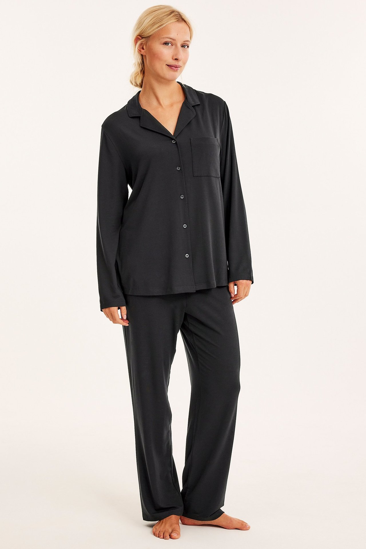 Widok z przodu: Kobieta w czarnej piżamie z lyocellu, z koszulą na guziki i prostymi spodniami.