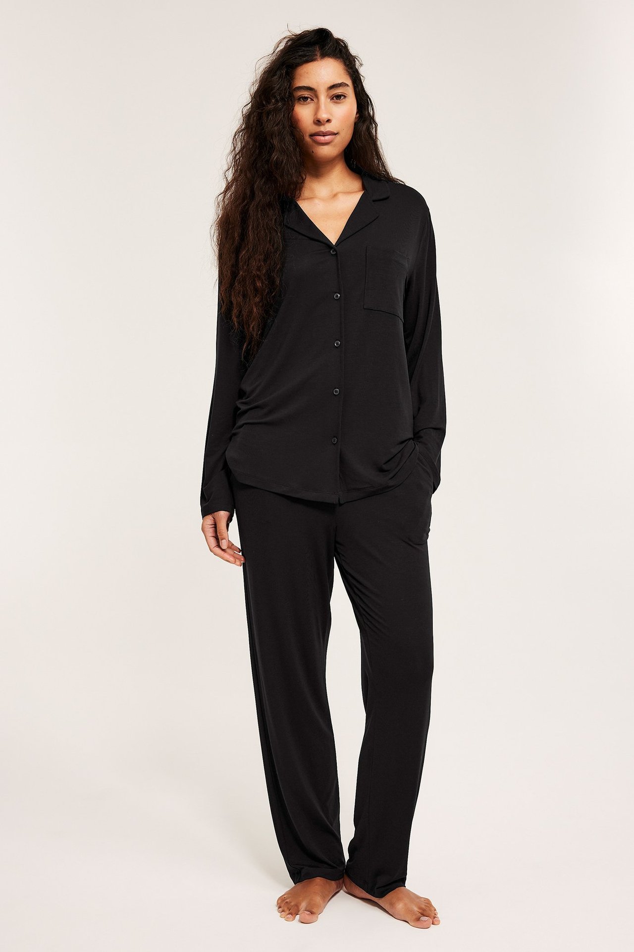 Widok z przodu kobiety w czarnej piżamie z lyocellu: koszula z kołnierzykiem na guziki, luźne proste spodnie.