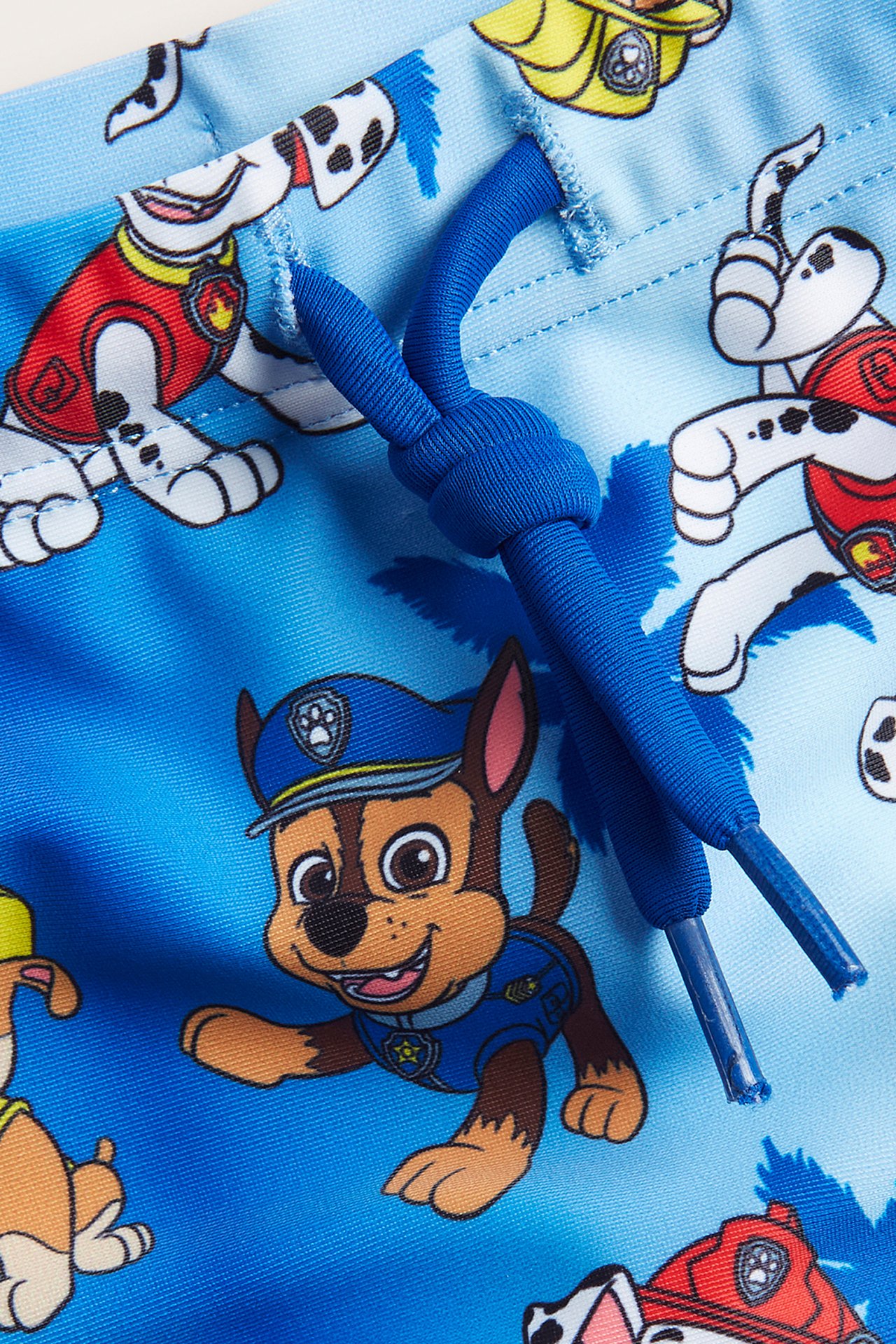 Zbliżenie na niebieskie kąpielówki dziecięce Psi Patrol z wzorem zwierzęcym i niebieskim sznurkiem.