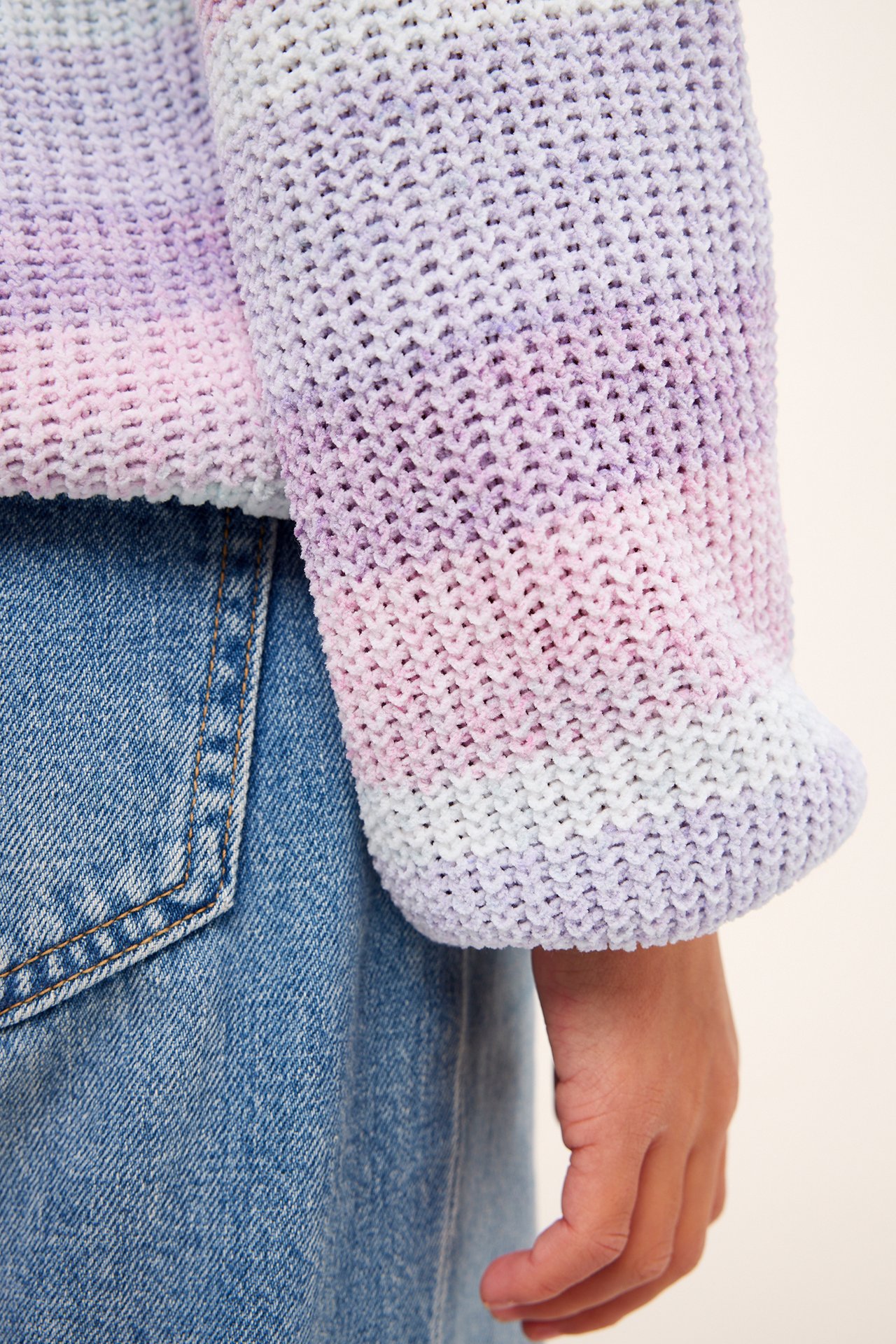 Närbild på ett barn i en regnbågsrandig stickad chenilletröja med blå jeans.