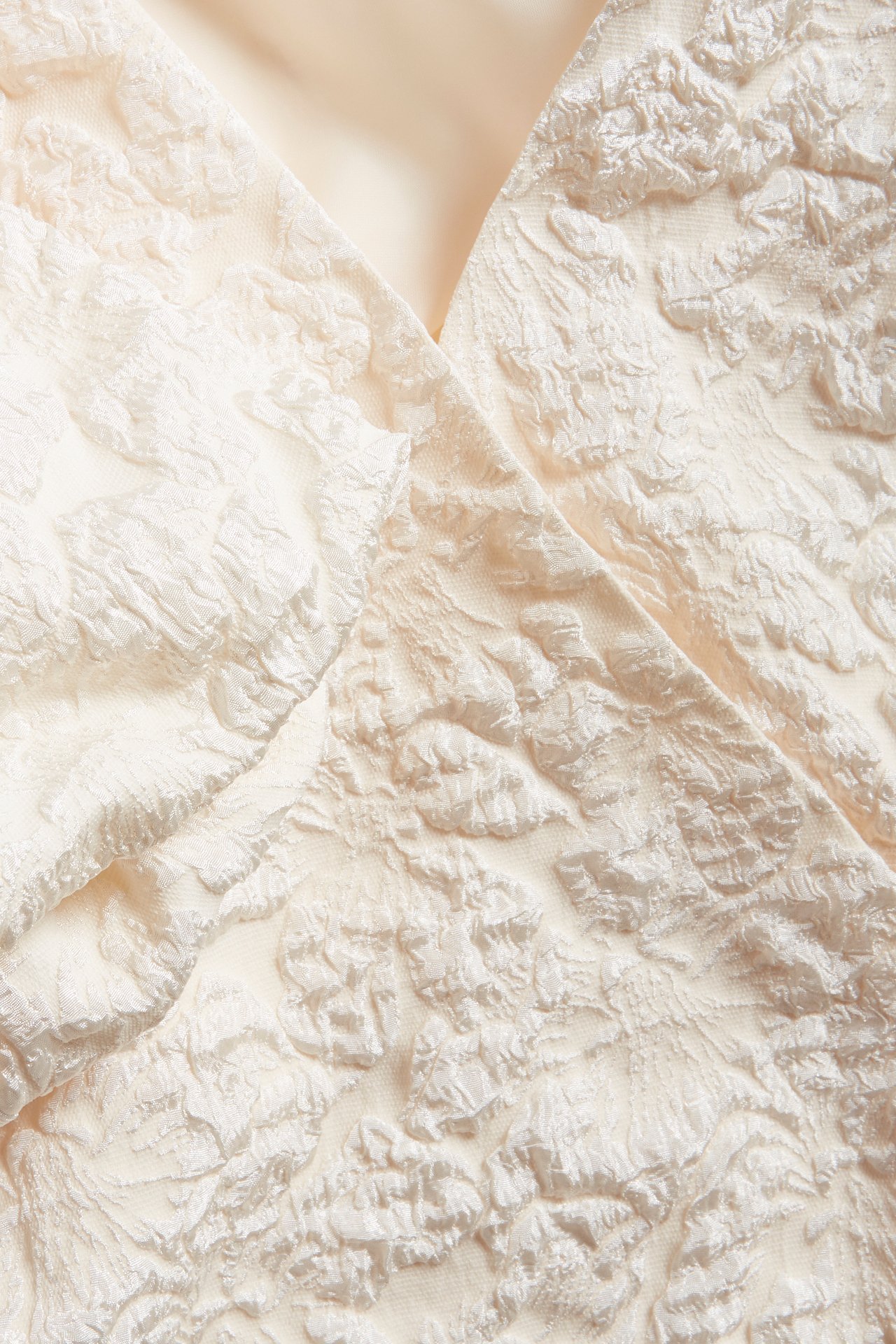 Närbild av en offwhite jacquard omlottklänning med texturerat mönster.