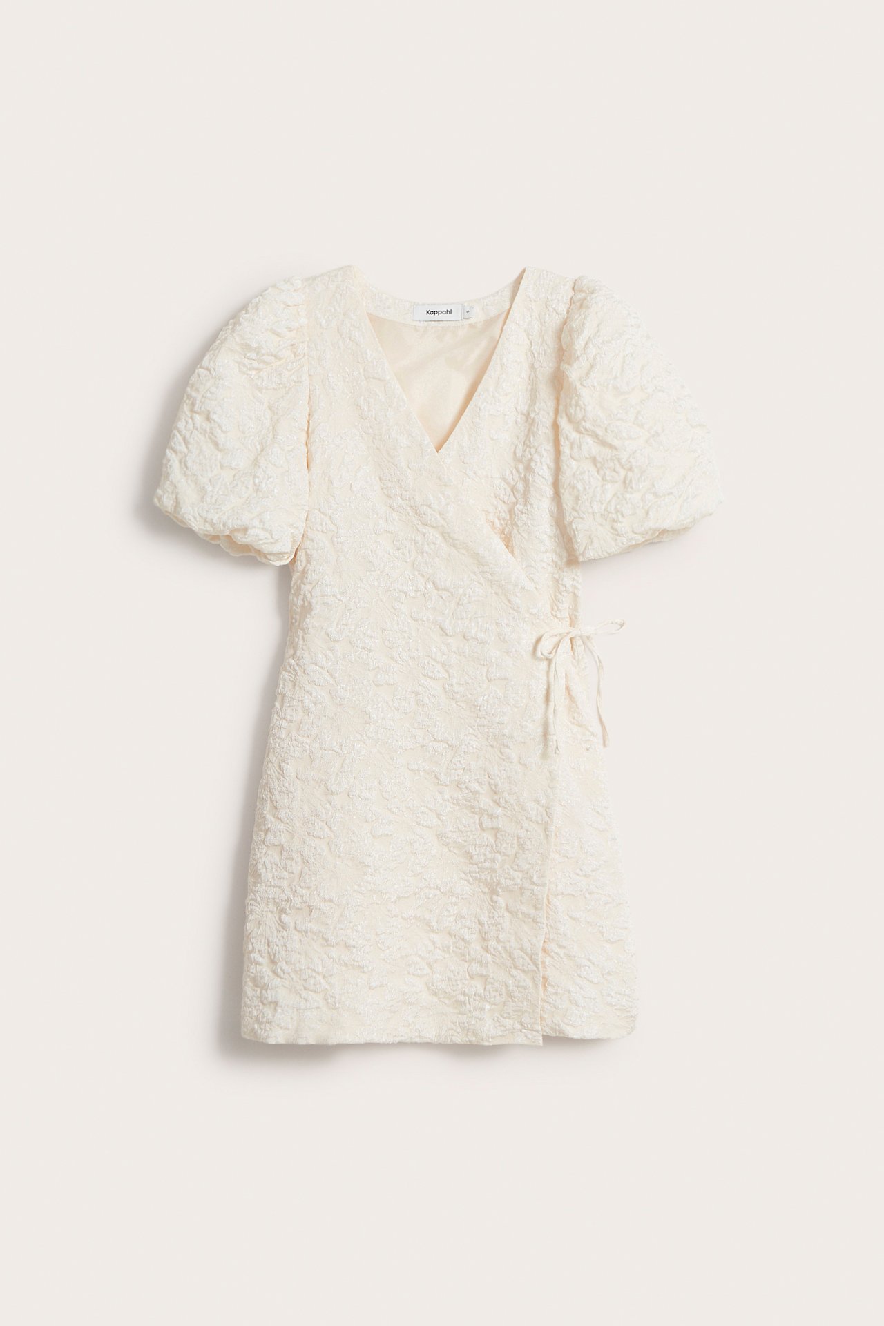 Framsida av en offwhite jacquard omlottklänning med puffärmar och knytband i sidan.