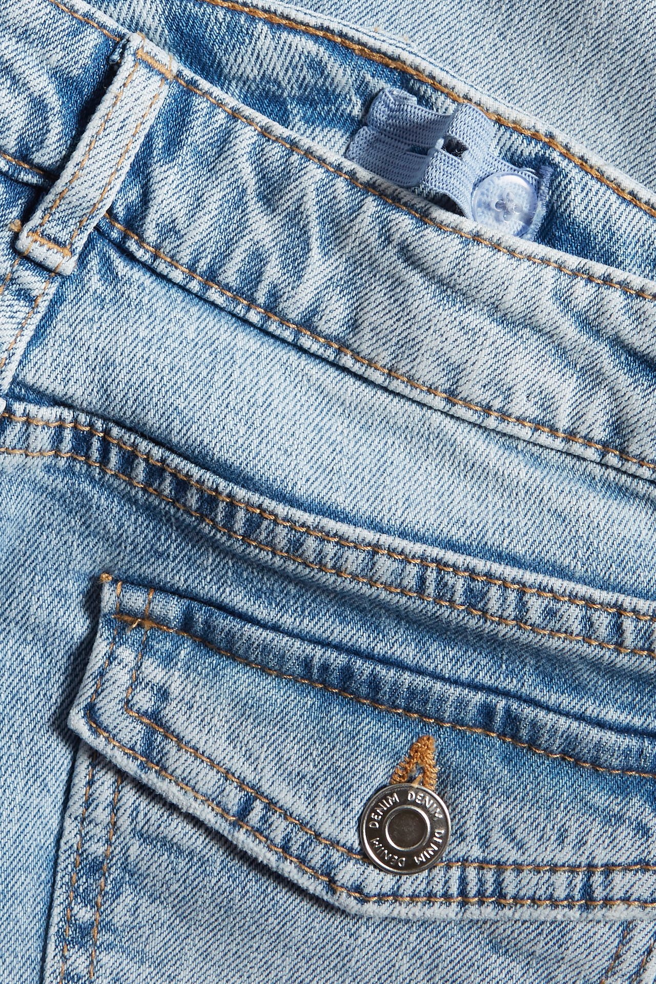 Lähikuva vaaleansinisistä bootcut-farkuista, joissa läppätasku ja säädettävä kuminauha vyötäröllä.