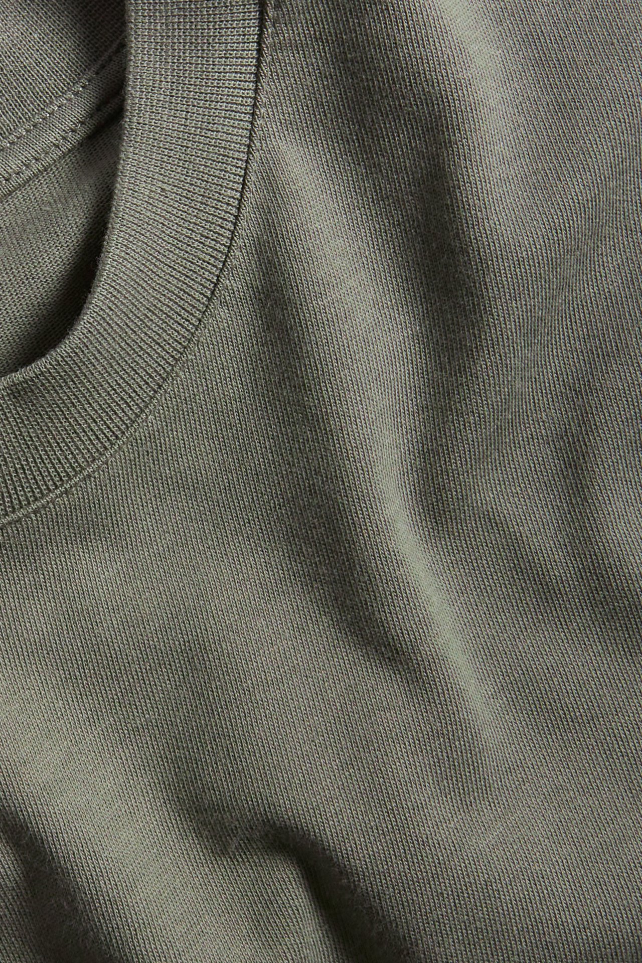 Zbliżenie na ciemnozielony, gładki, bawełniany t-shirt z okrągłym dekoltem o luźnym kroju i ściągaczem.
