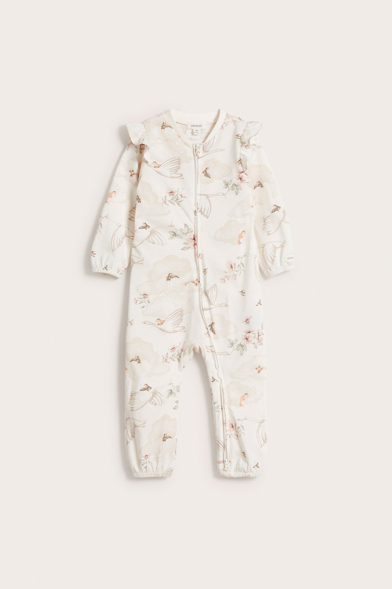 Edestä: Luonnonvalkoinen vauvan puuvillapyjama, jossa olkapäässä röyhelöt, kaksisuuntainen vetoketju ja lintu-kukkakuvio.