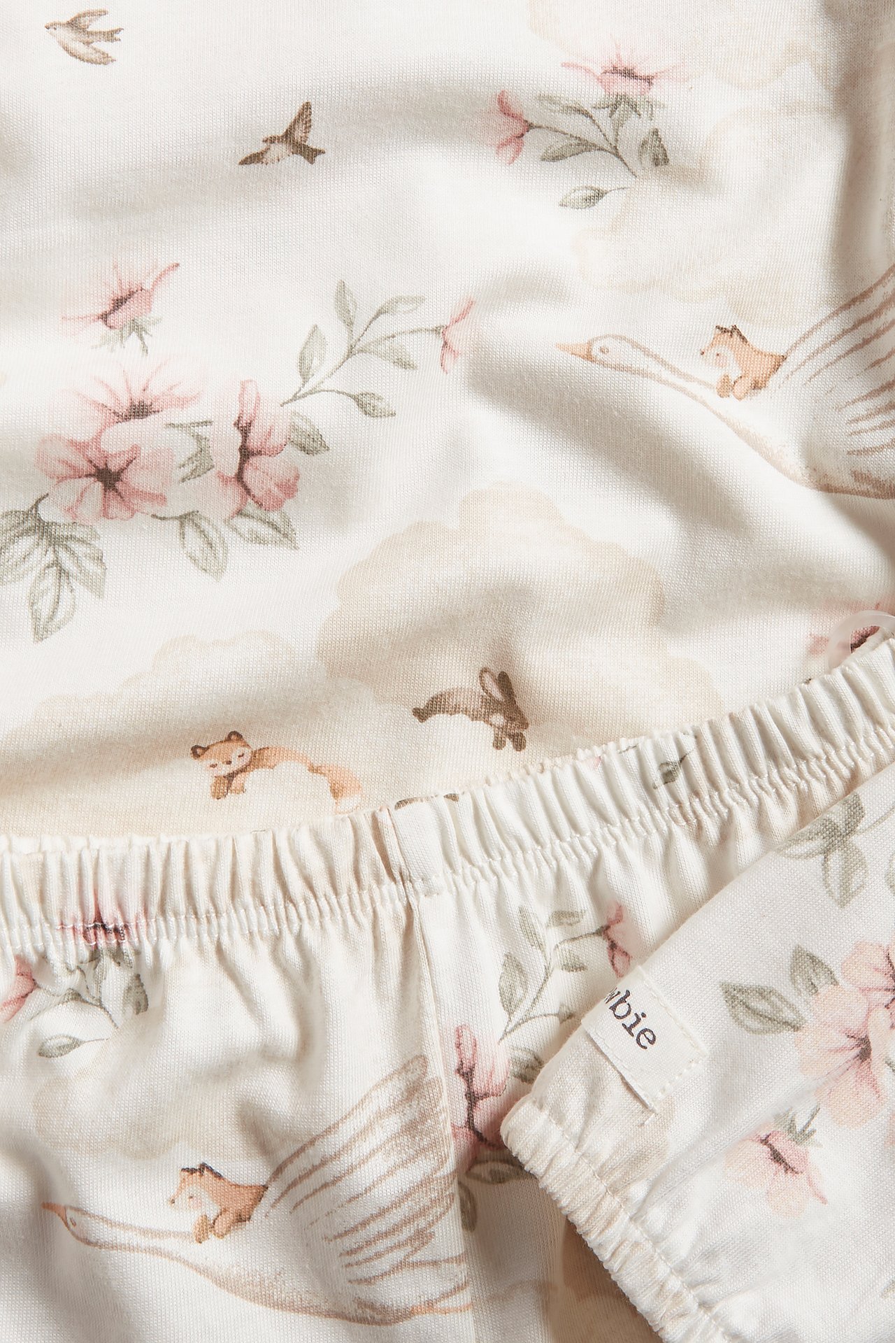 Närbild: offwhite barnpyjamas i bomull, mönstrad med blommor, blad, fåglar, kaniner och rävar på svanar.