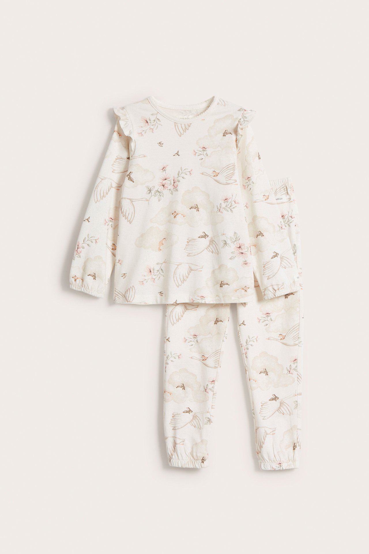 Framifrån: Offwhite pyjamas i bomull för barn med volanger, med svan-, moln- och blommönster.