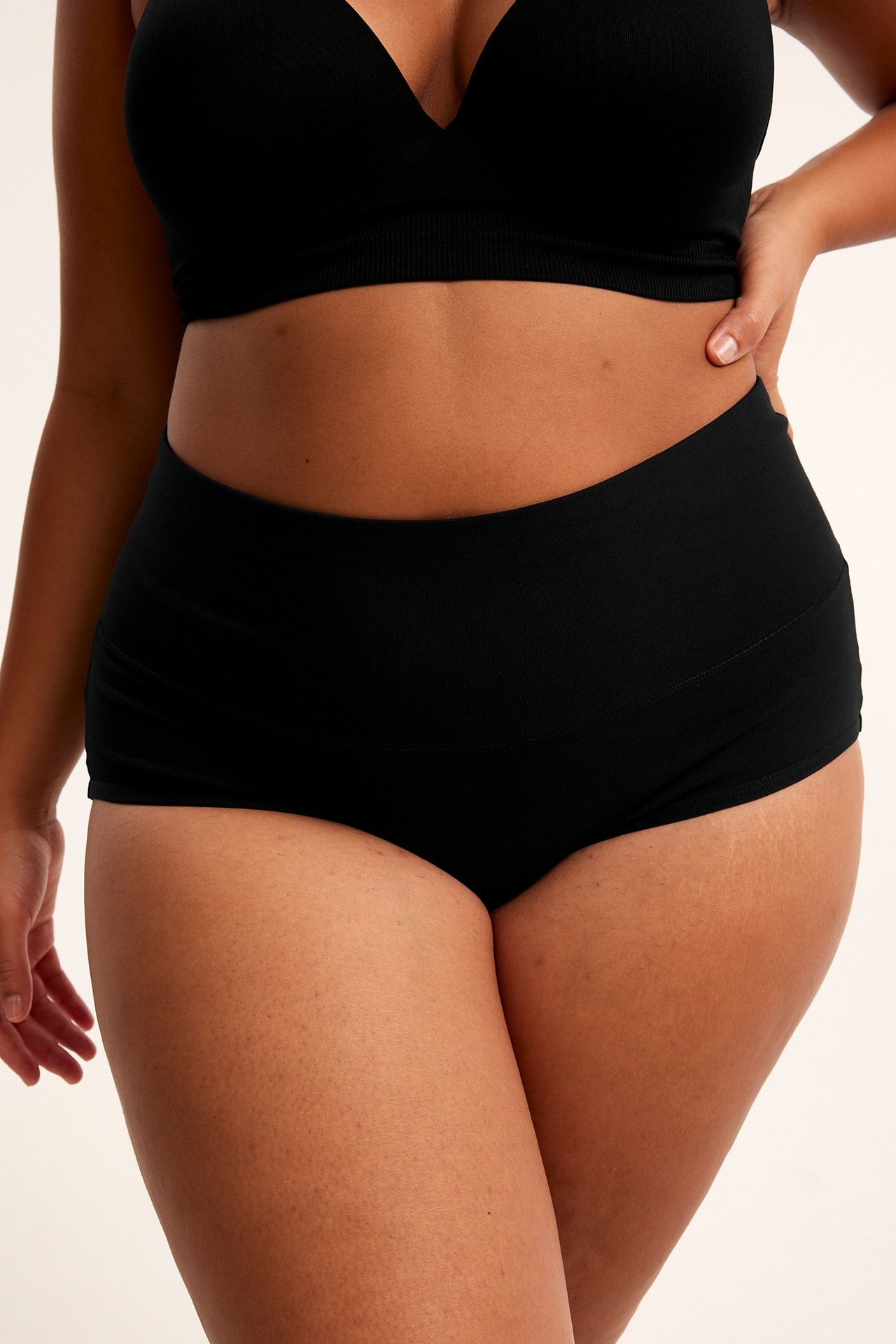 Edestä näkymä naisesta, jolla on mustat pehmeät puuvillahipsterit leveällä vyötärönauhalla ja mustat rintaliivit.