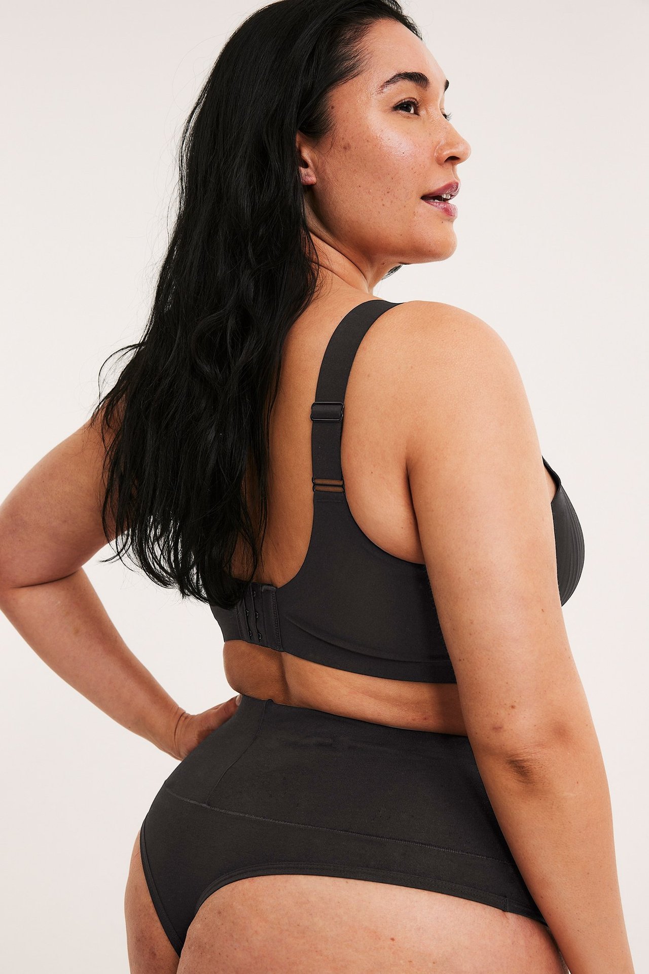 Sivukuva naisesta, jolla on mustat puuvillastrongit leveällä vyötärönauhalla ja yhteensopivat mustat rintaliivit.