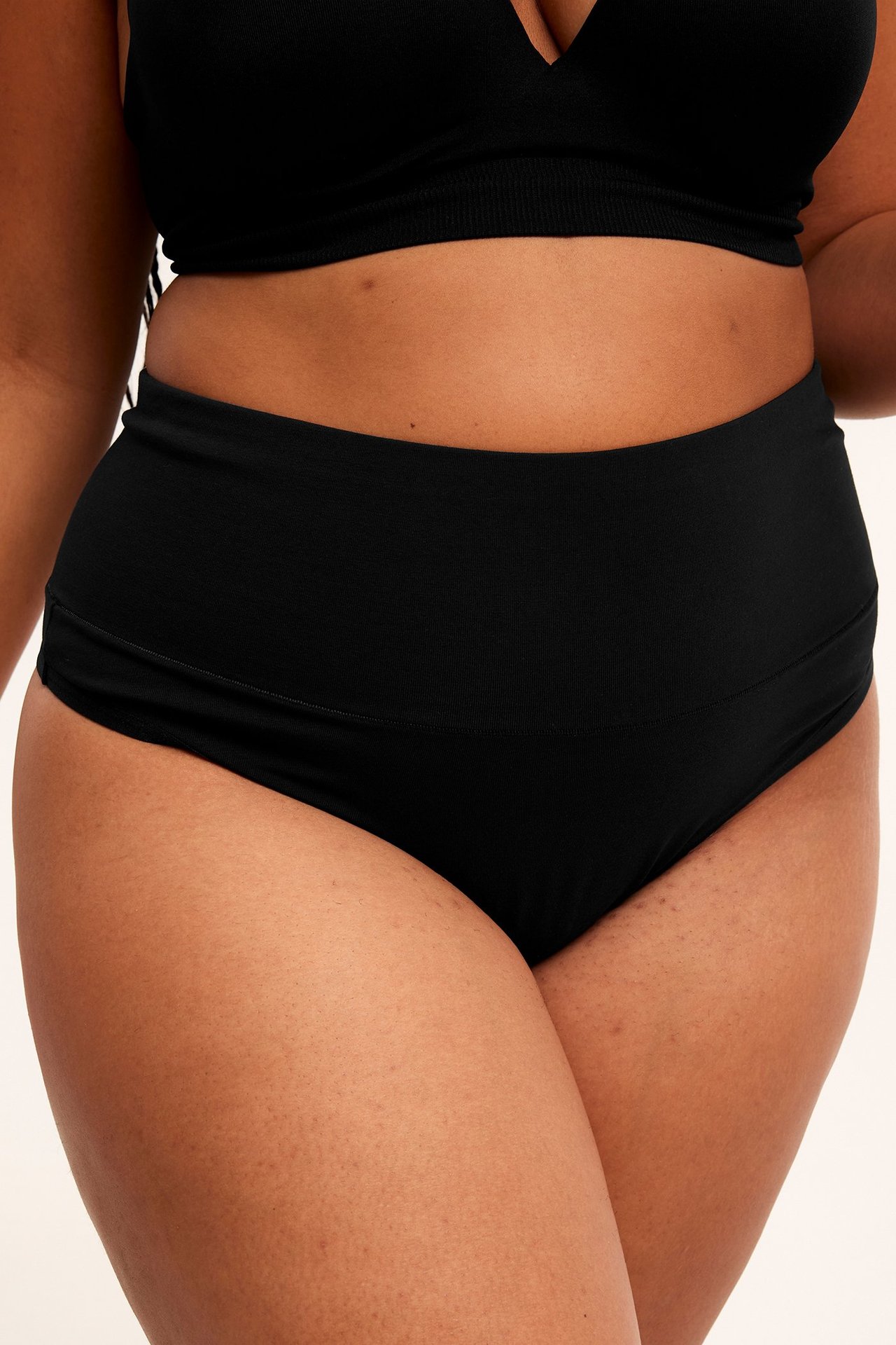 Edestä, nainen yllään mustat korkeavyötäröiset puuvillasekoitestringit ja musta rintaliivitoppi.