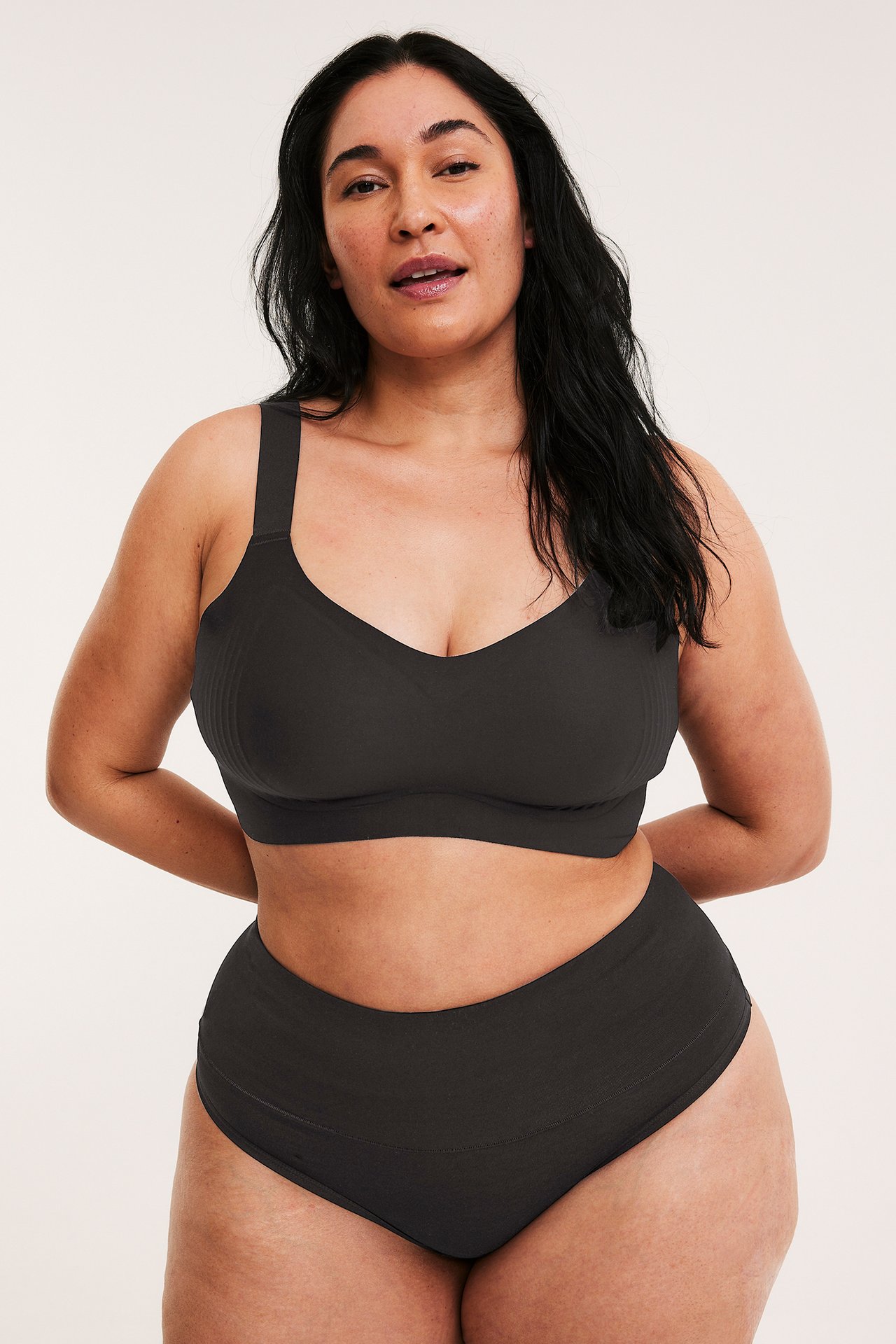 Nainen edestä mustissa puuvillastringeissä leveällä vyötärönauhalla ja yhteensopivassa bralettessa.