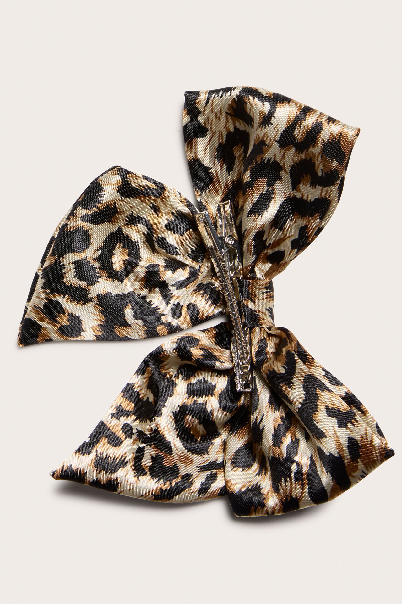 Närbild av en stor ljusbeige leopardmönstrad rosett hårklämma i polyester med silverfärgad metallklämma.
