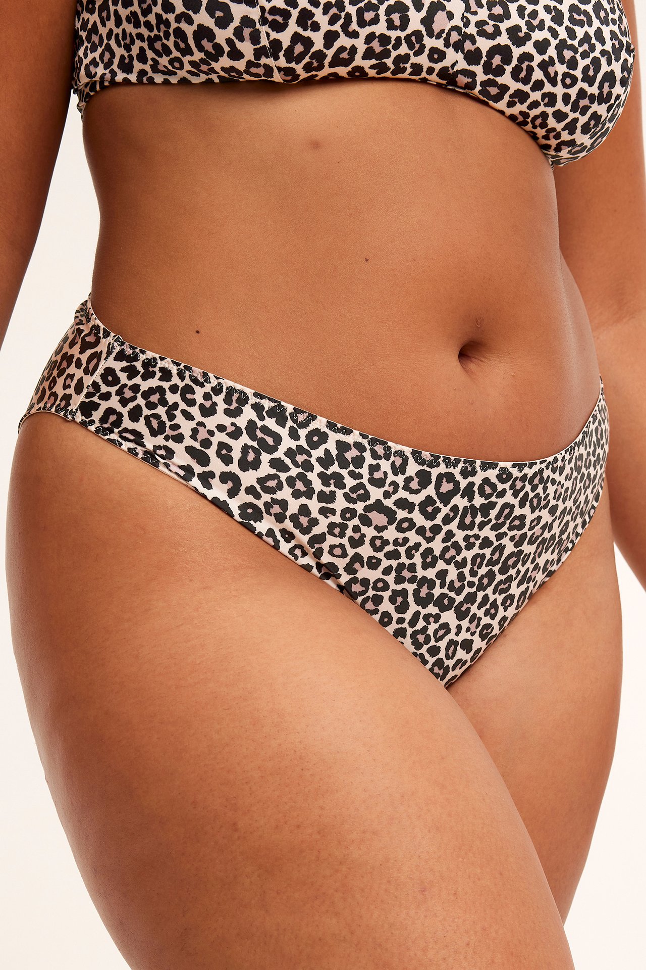 Närbild framifrån på en kvinna i beige leopardmönstrad brazilian trosa i stretchsatin och matchande BH.