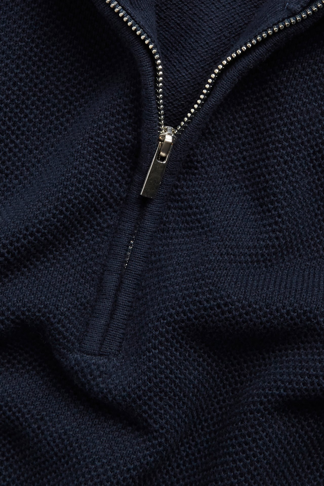 Zbliżenie na granatowy bawełniany sweter half-zip ze wzorem strukturalnym i srebrnym zamkiem błyskawicznym.