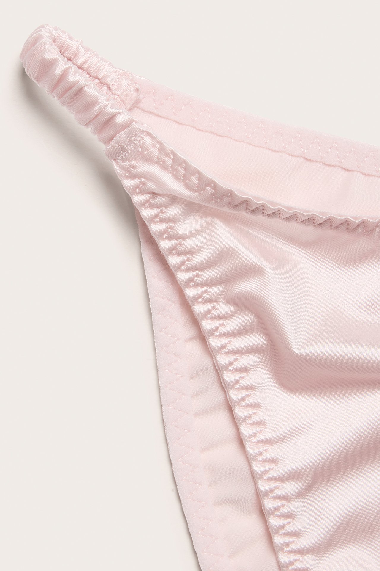 Nærbilde av en rosa sateng Brazilian-truse med smale rynkede sidebånd.