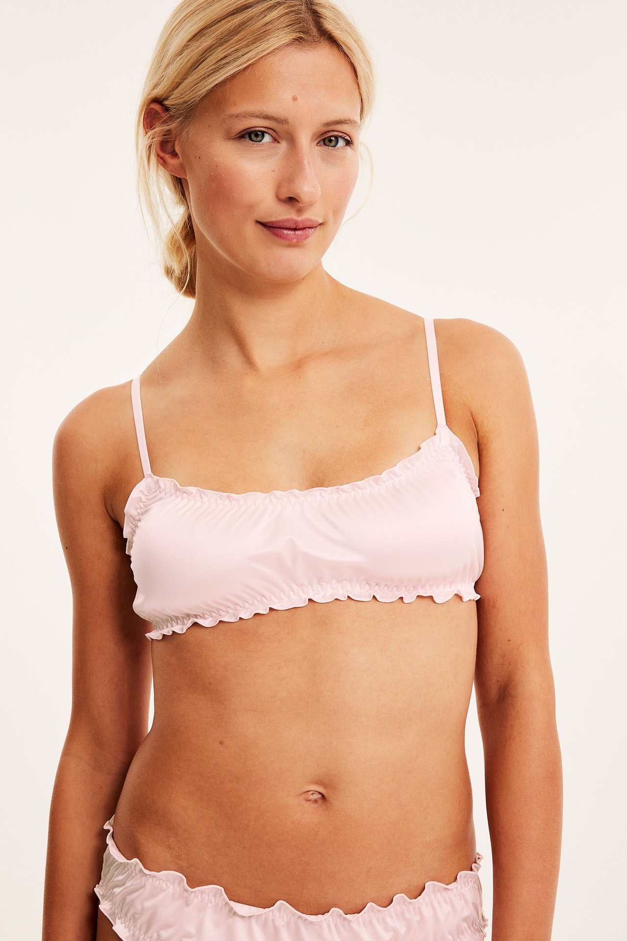 Frontvy av en kvinna som bär en rosa satinbralette med volangkanter och matchande trosor.