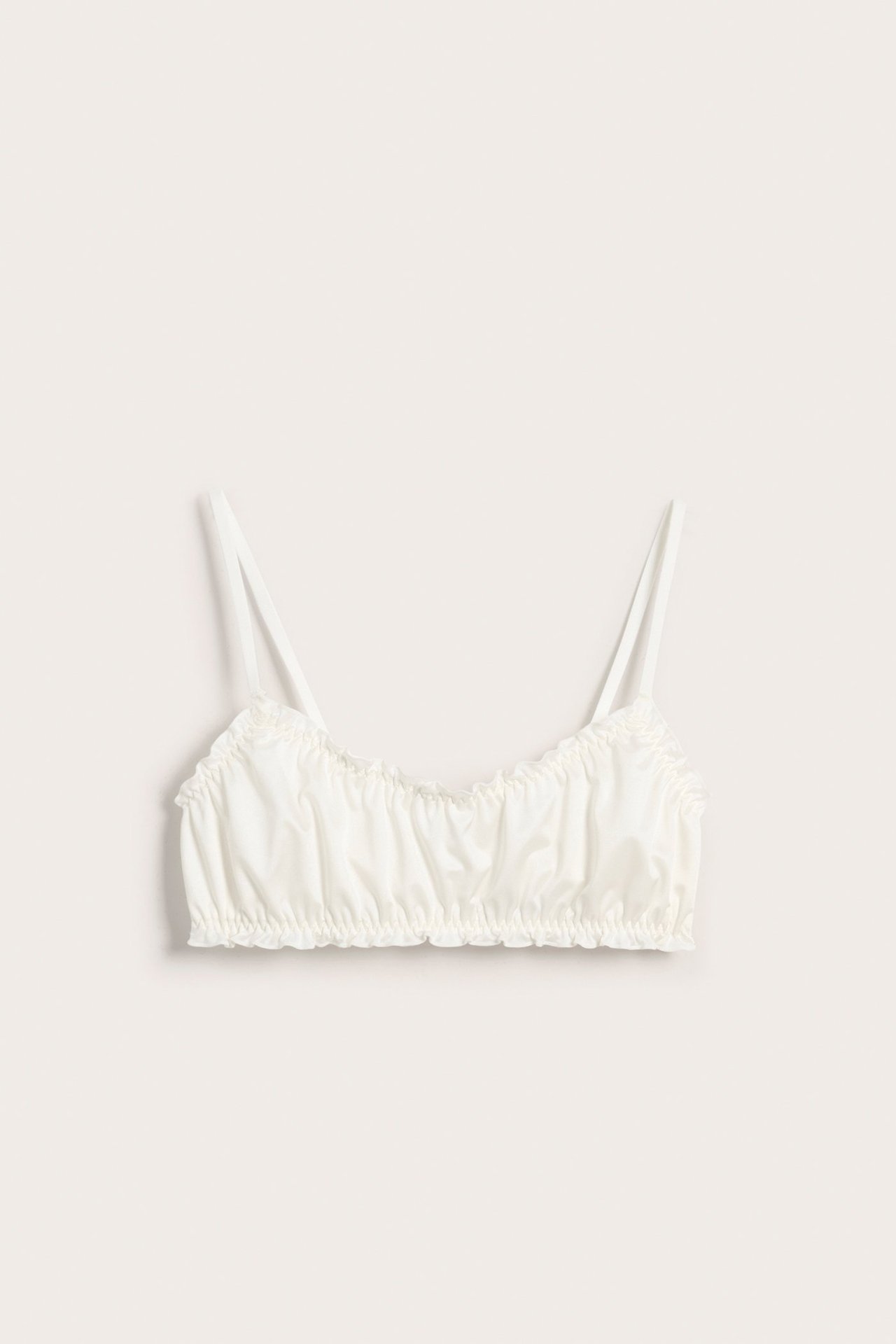 Frontvy av en offwhite satinbralette med rynkade kanter och tunna axelband.