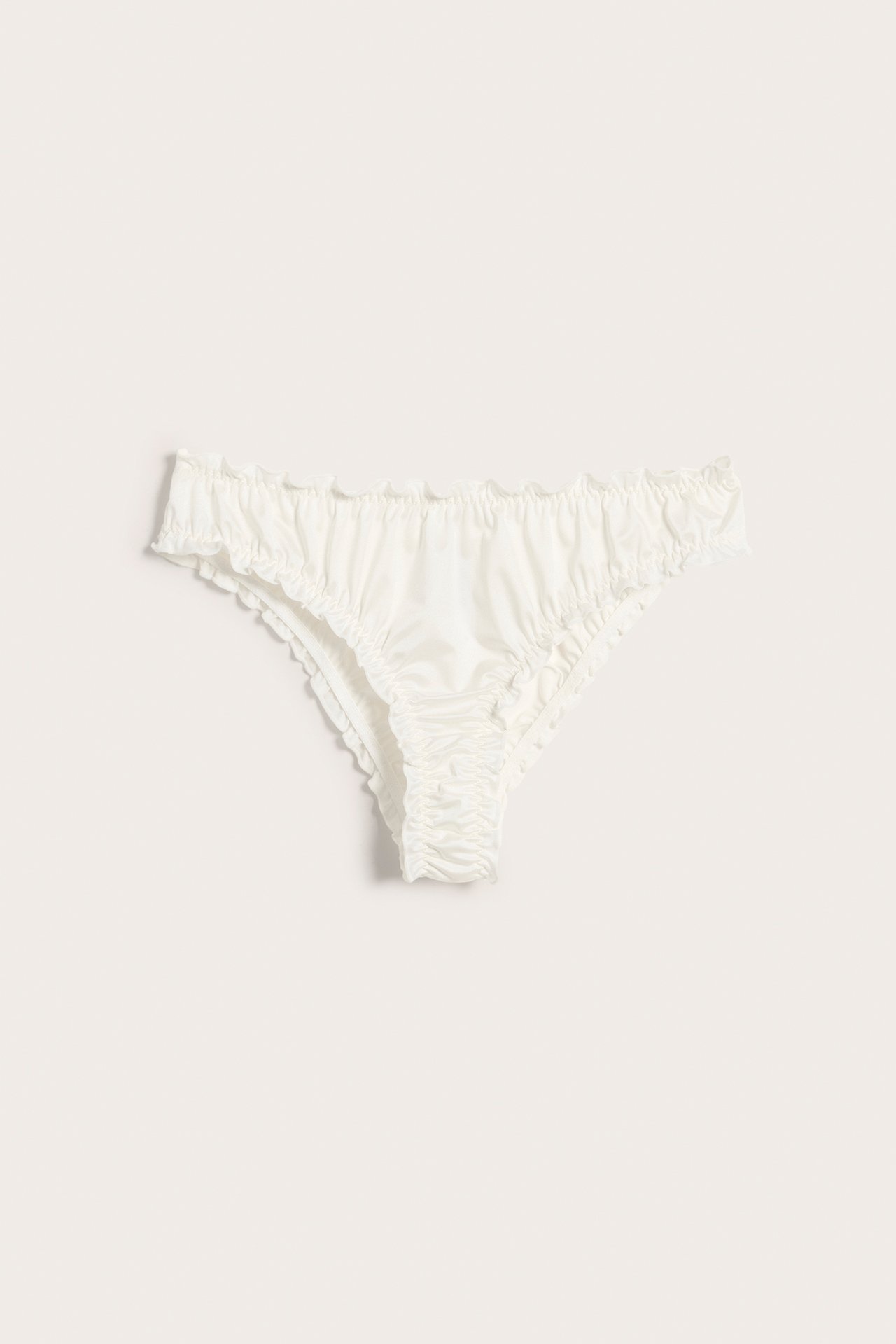 Frontvisning: Offwhite sateng Brazilian truse med volangkanter og rynket detalj.