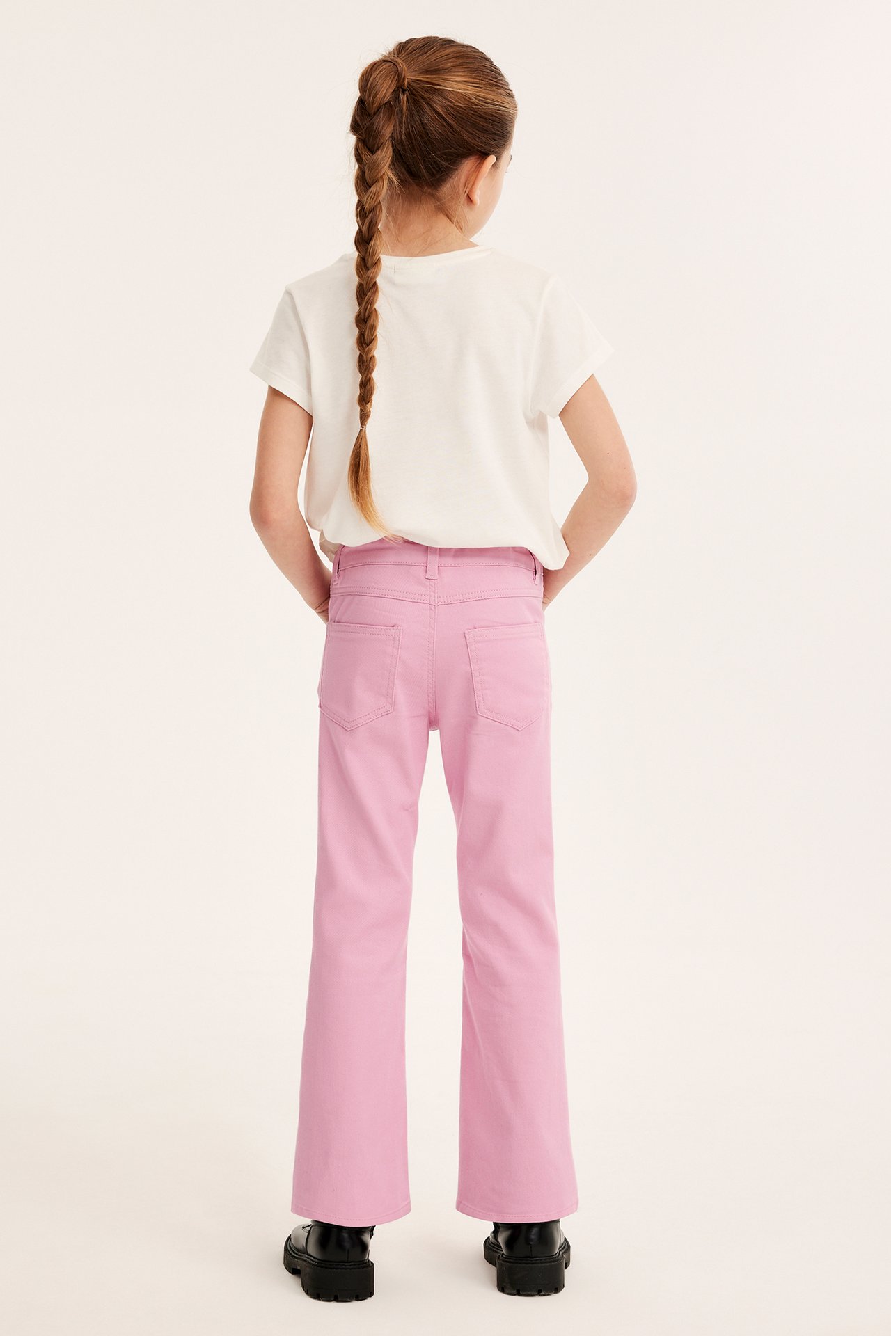 Bakifrån: ett barn i rosa bootcut-jeans, en vit t-shirt och svarta skor.