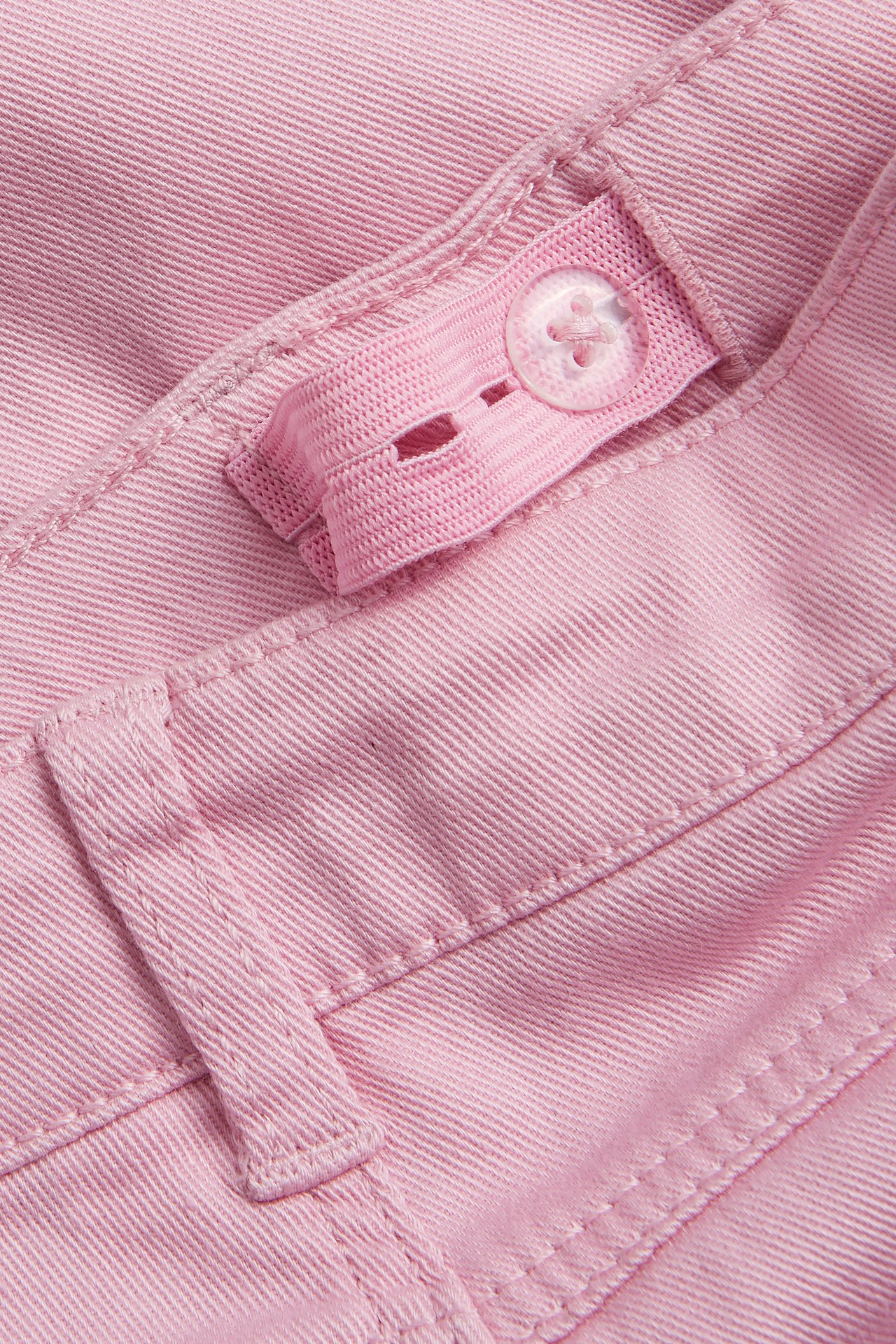 Närbild av rosa bootcut-jeans med justerbar resår i midjan och en genomskinlig knapp.