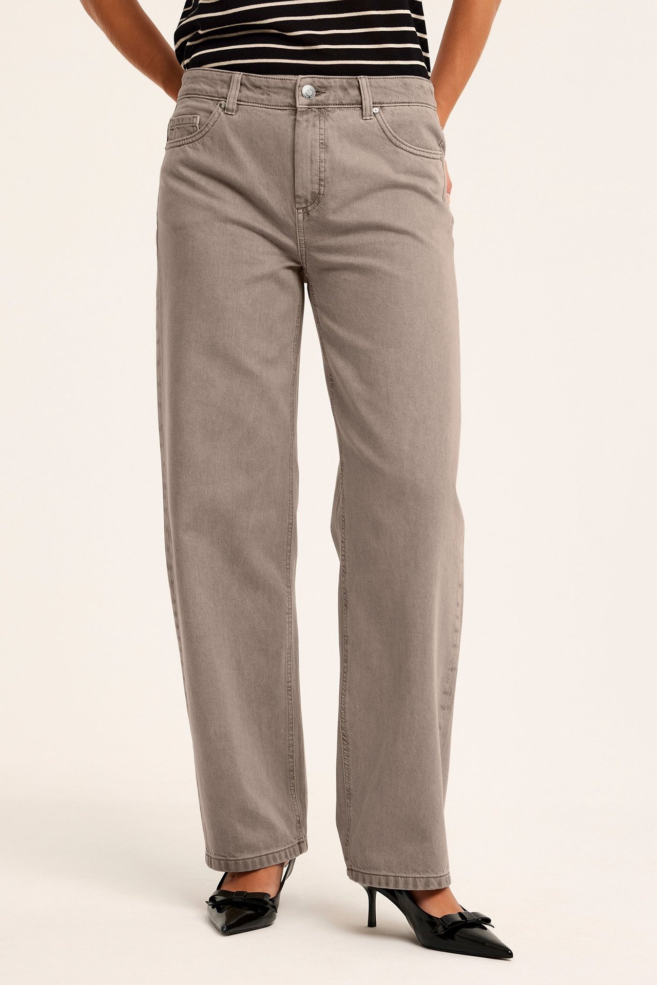 Framifrån: Kvinna i ljusbruna baggy jeans, randig topp och svarta högklackade skor med rosett.