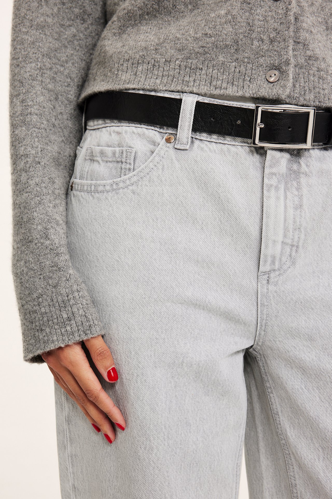 Närbild på kvinna i ljusgrå baggy jeans, svart bälte och grå stickad kofta.