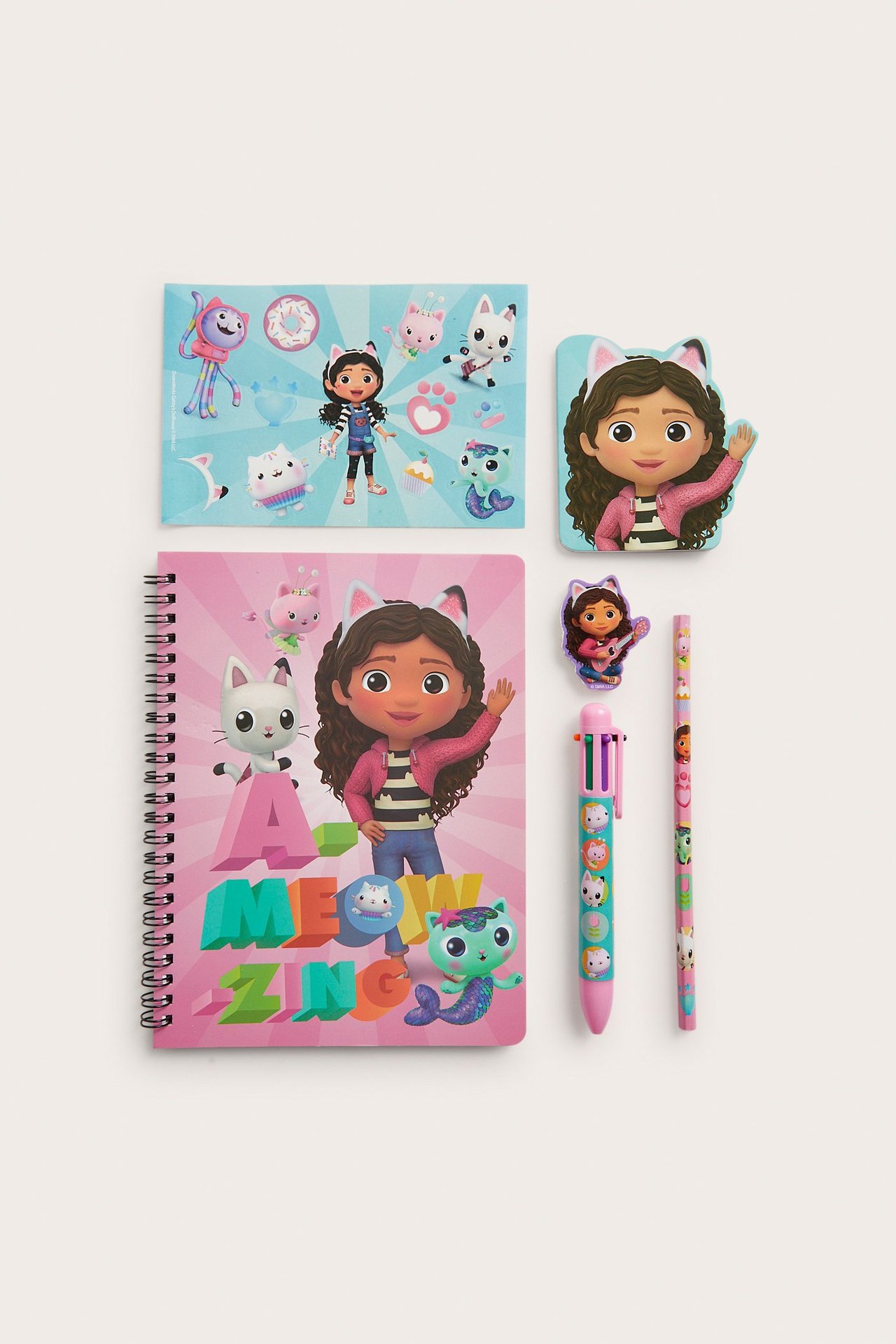 Widok z góry: różowy zeszyt spiralny Gabby's Dollhouse, niebieski notatnik, gumka, naklejka, długopis wielokolorowy i ołówek.