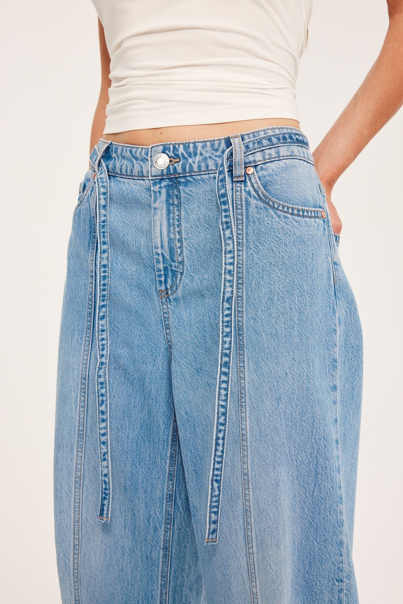 Kvinne i lyseblå vide jeans med høyt liv, frontsømmer, knytebelter og en hvit crop top.