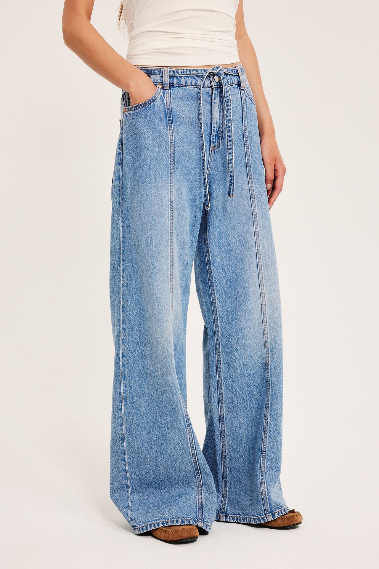 Framifrån: kvinna i ljusblå vida jeans med hög midja, frontsömmar och vit topp.
