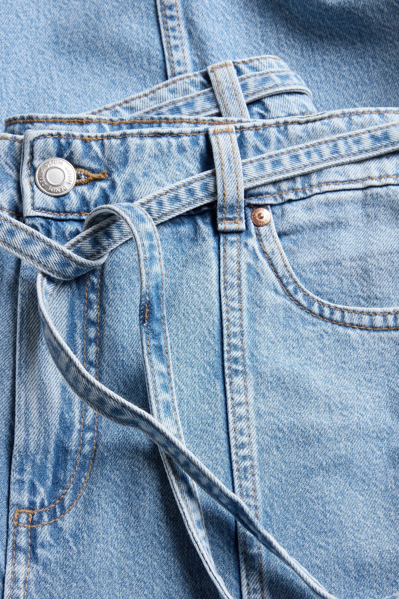 Zbliżenie jasnoniebieskich szerokich jeansów z wysokim stanem, szwem z przodu i wiązanym paskiem.