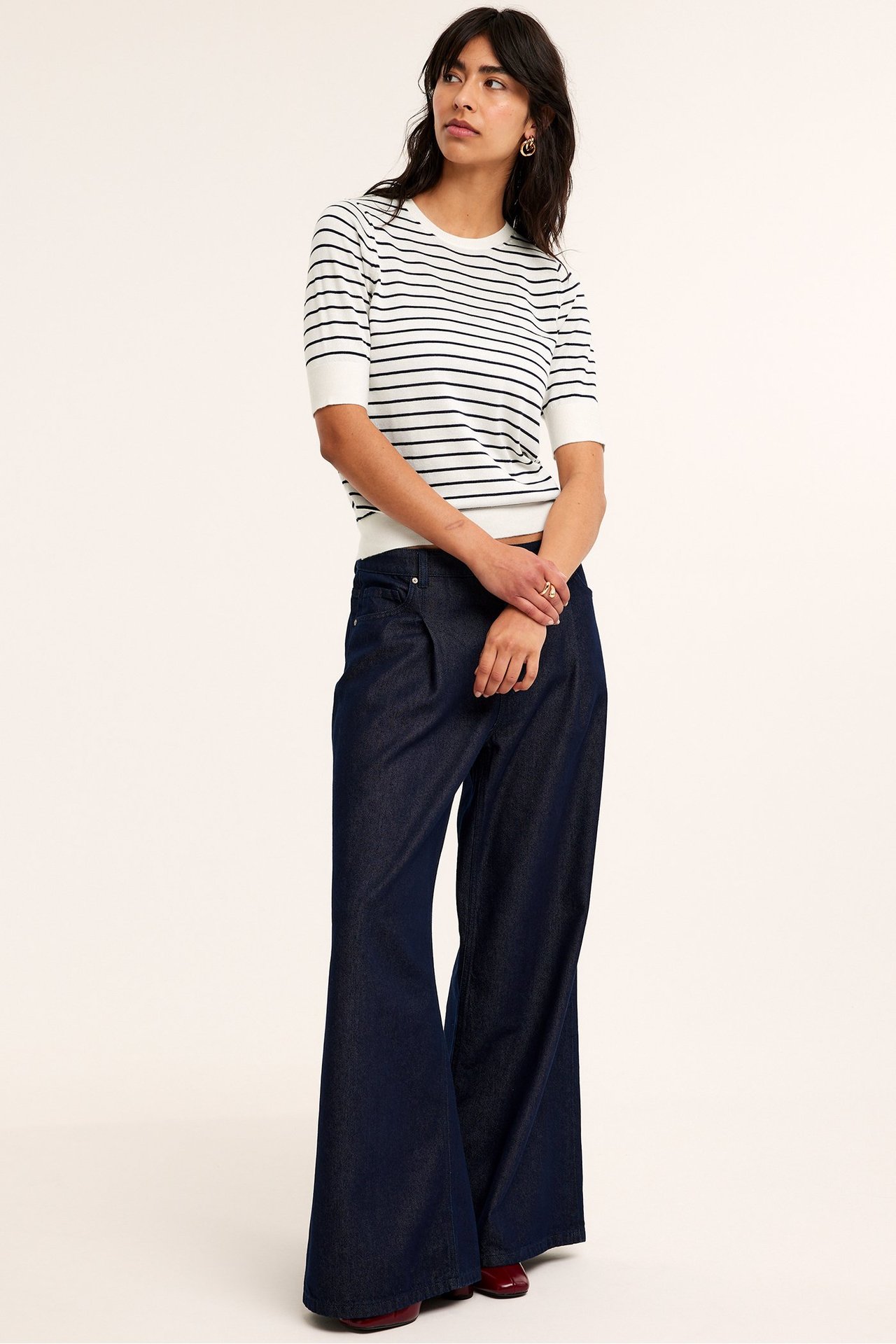 Edestä: nainen valkoisessa raidallisessa lyhythihaisessa neulepuserossa ja tummansinisissä leveissä farkuissa.