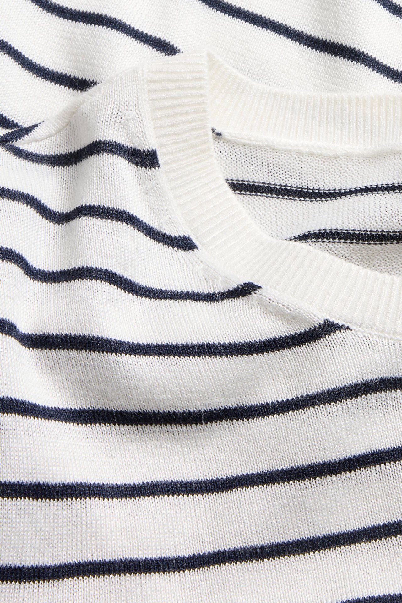 Zbliżenie białego, drobno dzianego swetra w ciemne poziome paski z prążkowanym dekoltem.