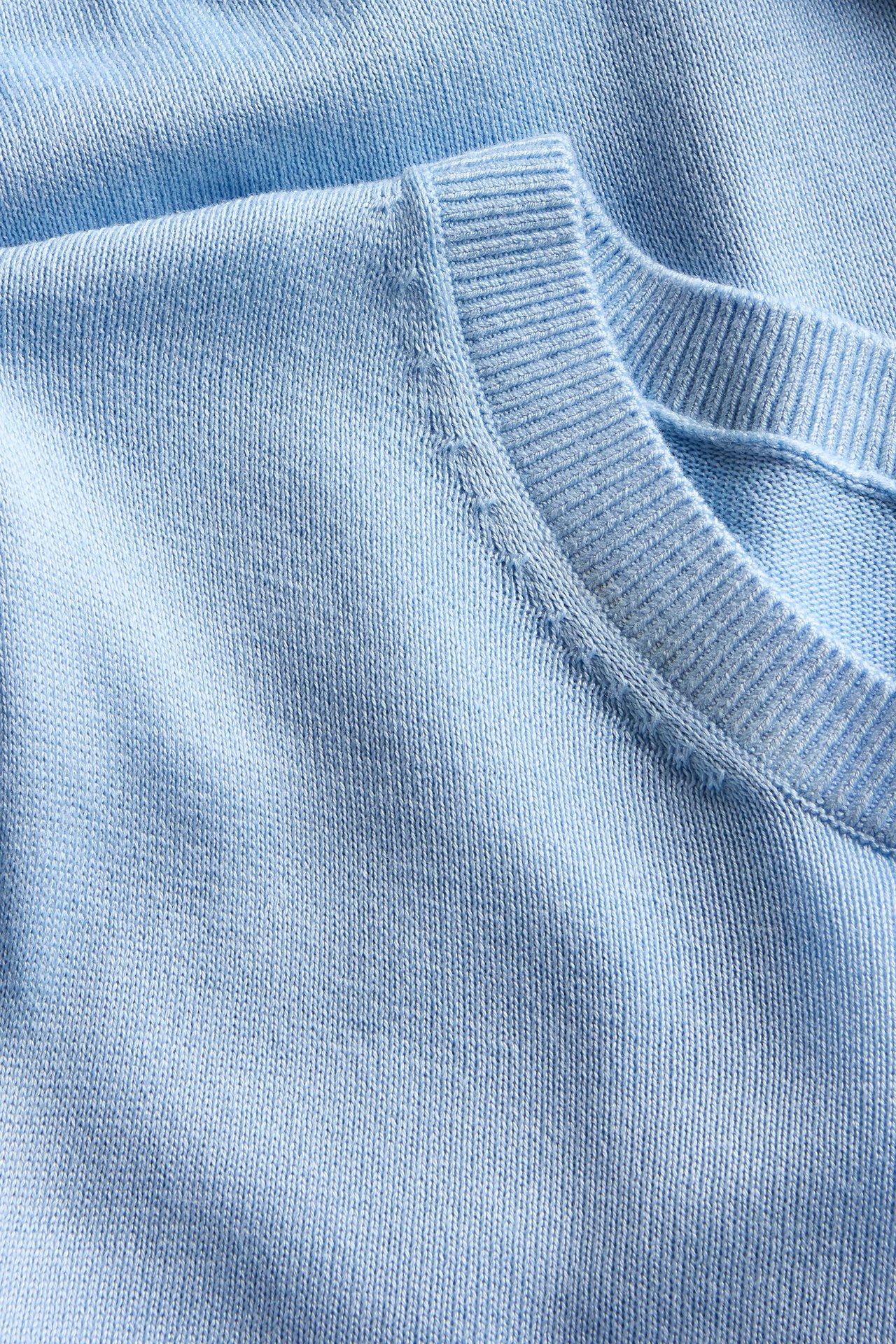 Zbliżenie na jasnoniebieski, cienki sweter z dzianiny, z prążkowanym dekoltem i szwem na ramieniu.