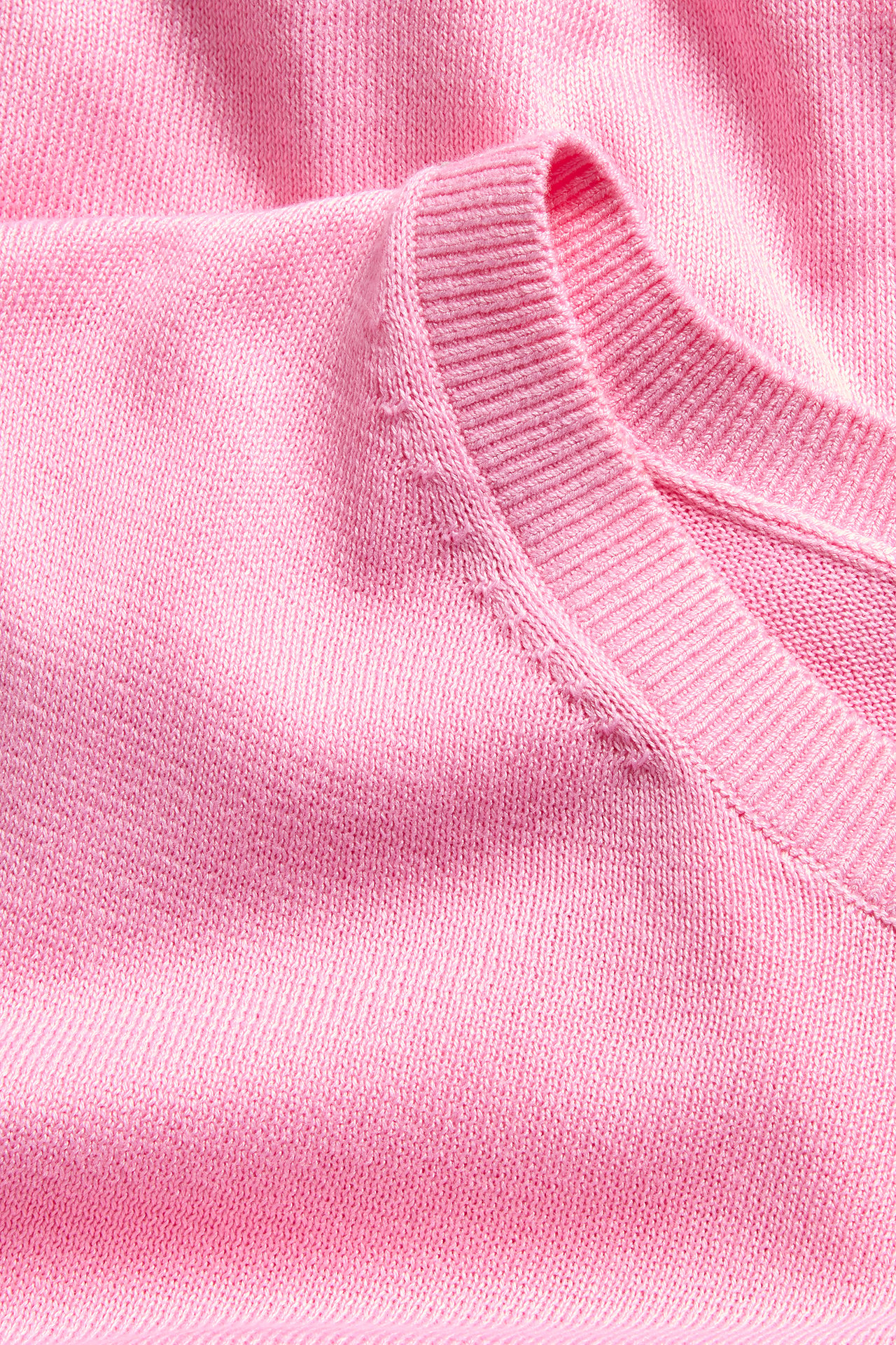 Närbild av en rosa finstickad V-ringad tröja med ribbad kant.