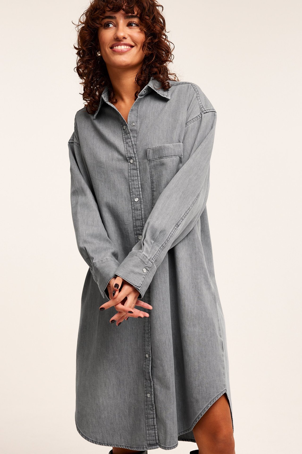 Frontvy av en kvinna i en lång, avslappnad grå jeansskjortklänning med krage och knappar.