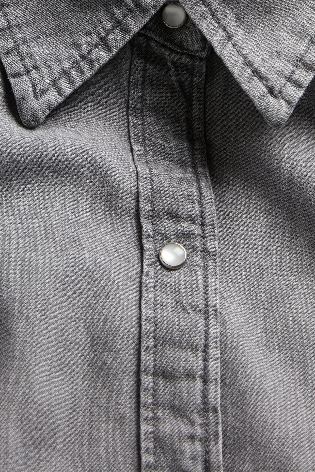 Zbliżenie szarej dżinsowej sukienki koszulowej z klasycznym kołnierzem i perłowym zatrzaskiem.