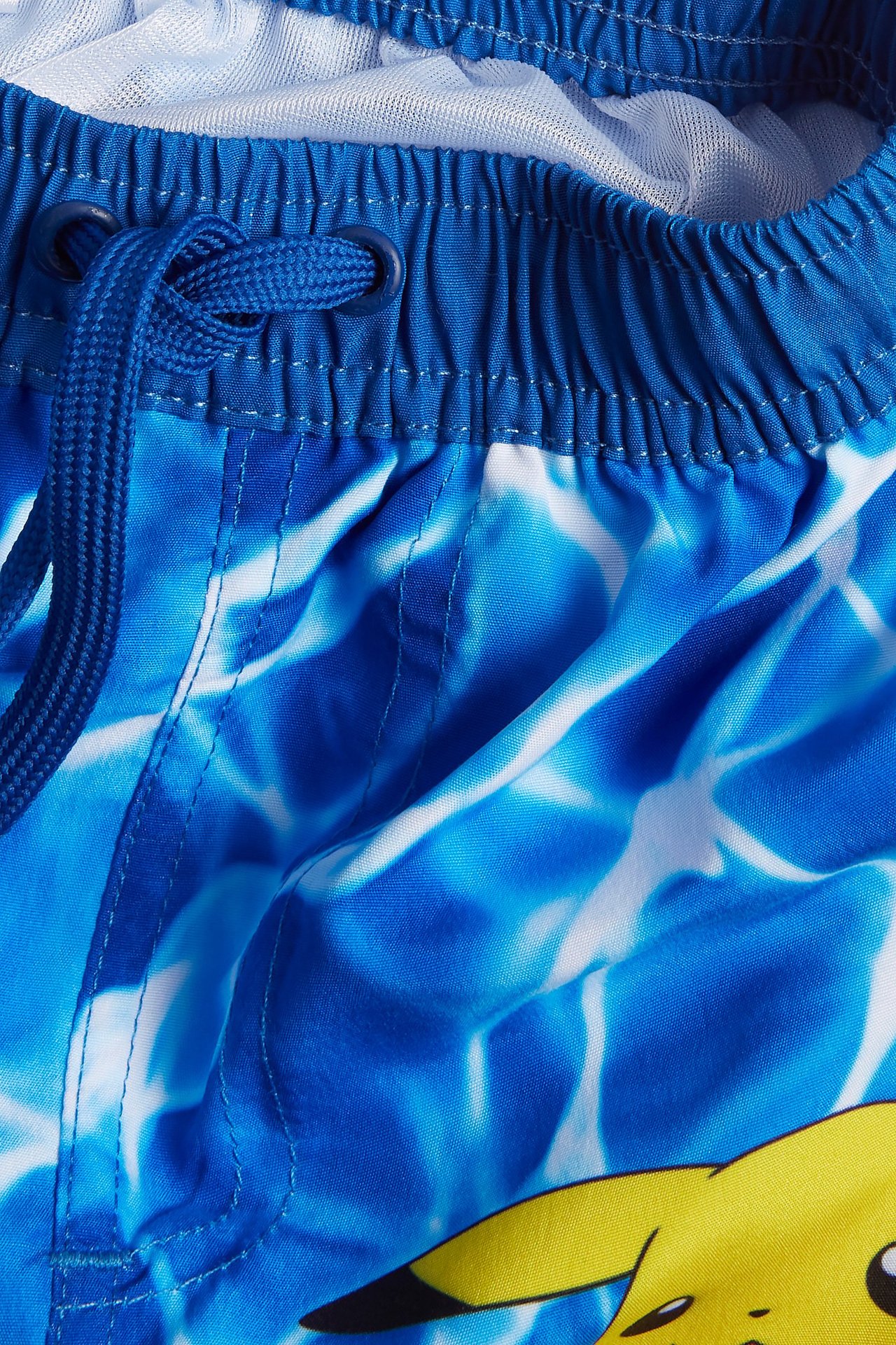 Närbild på barnens blå- och vitmönstrade badshorts med resårlinning, dragsko och Pikachu-tryck.