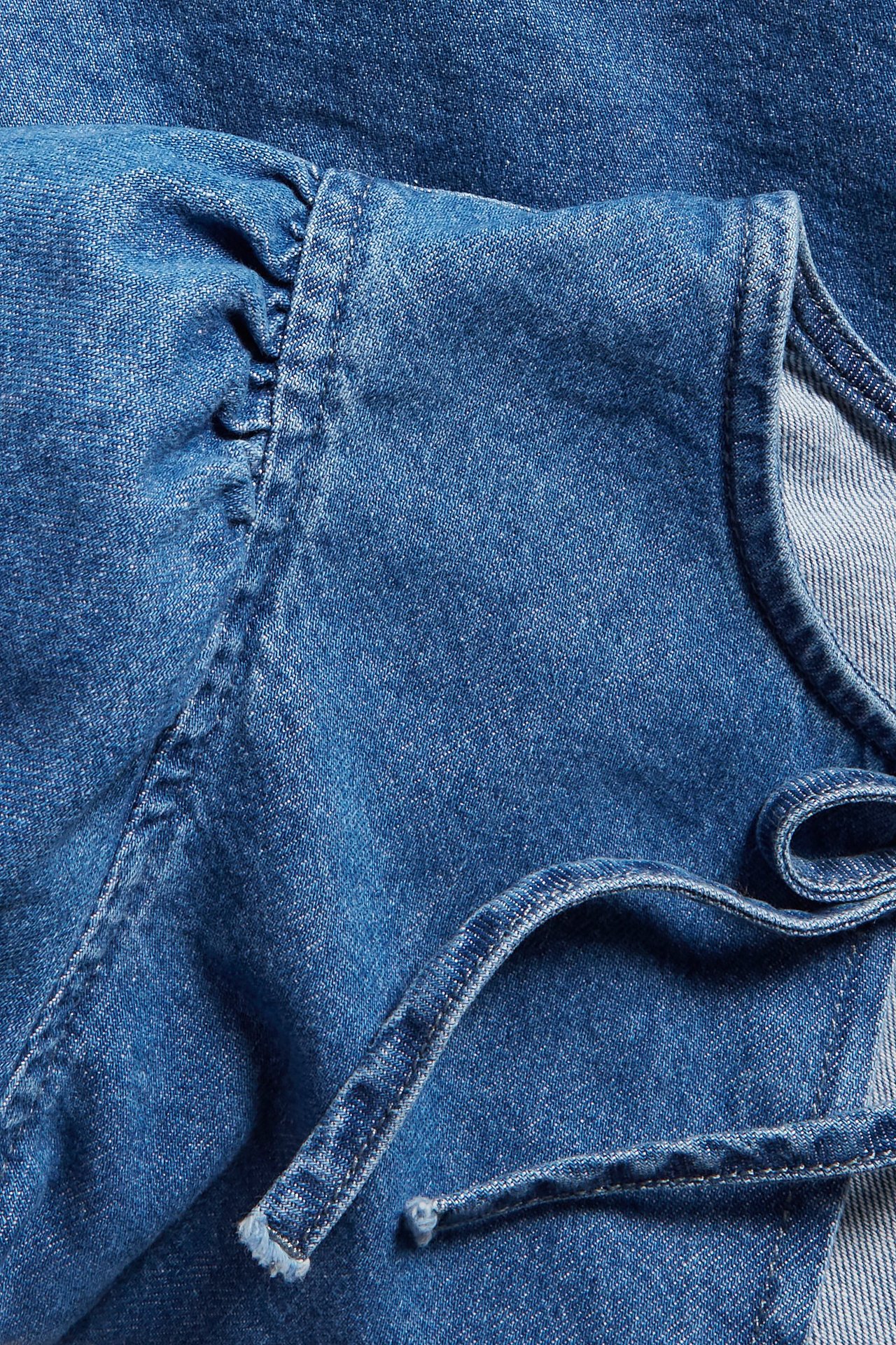 Zbliżenie niebieskiej bluzki jeansowej z bufiastymi rękawami i wiązaniem z przodu.