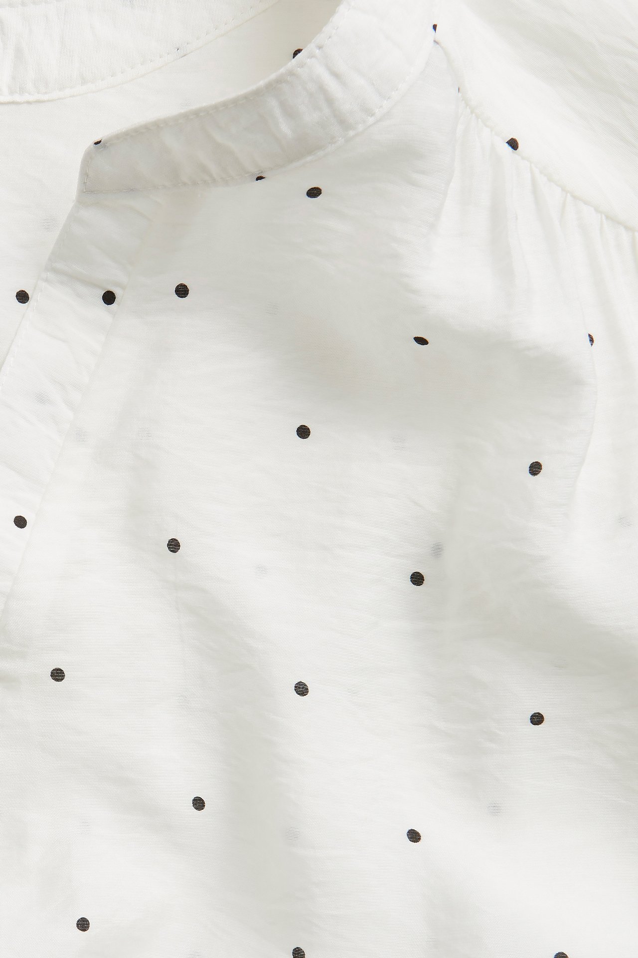 Närbild av en offwhite texturerad blus med svarta prickar och ståkrage.