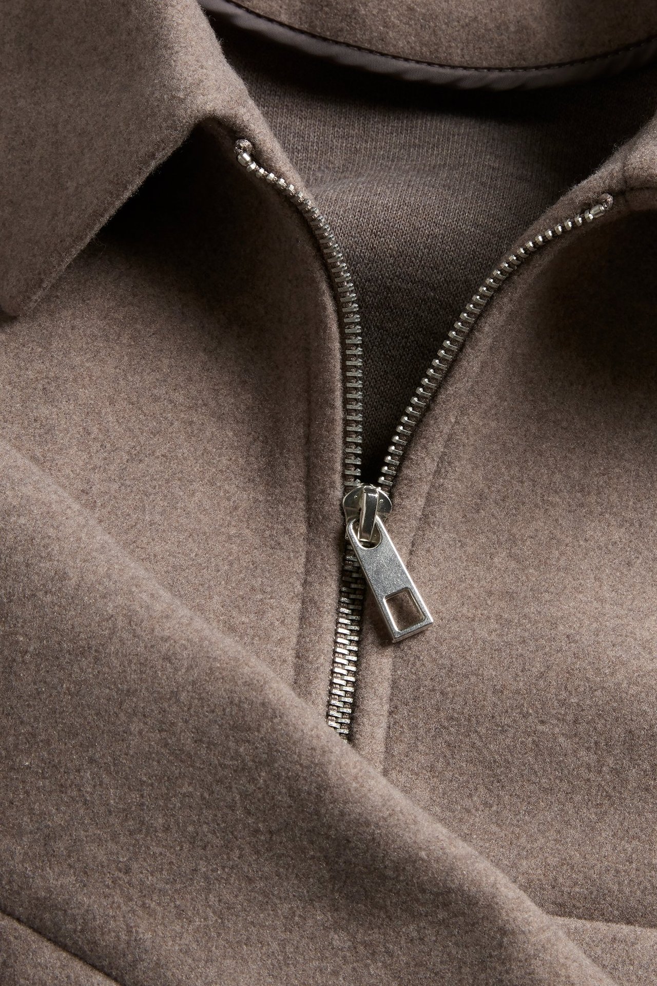 Zbliżenie beżowo-melanżowej filcowej kurtki ze srebrnym zamkiem błyskawicznym.