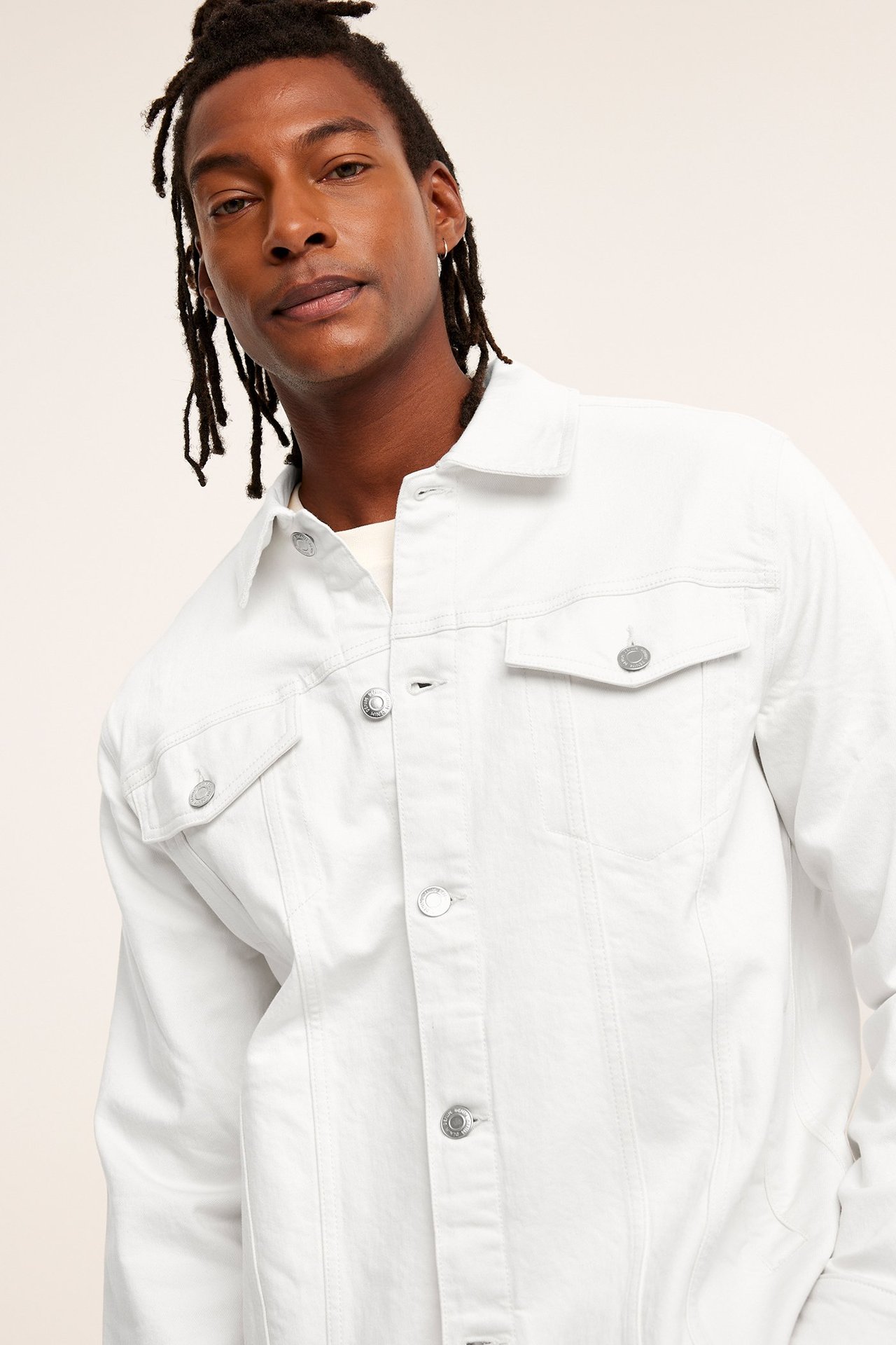 Edestä: mies beigessä twill-farkkutakissa, jossa napit ja rintataskut, vaalean t-paidan päällä.