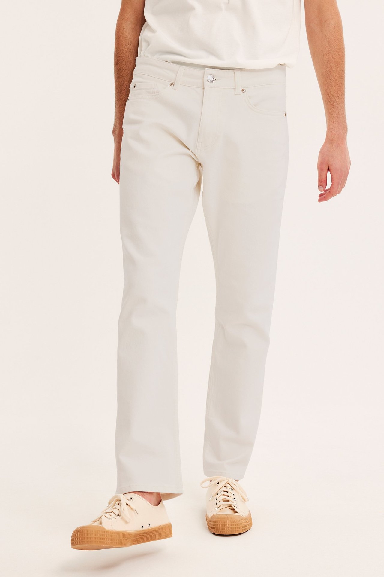 Edestä kuvattu mies yllään luonnonvalkoiset regular-farkut, valkoinen t-paita ja beiget tennarit.